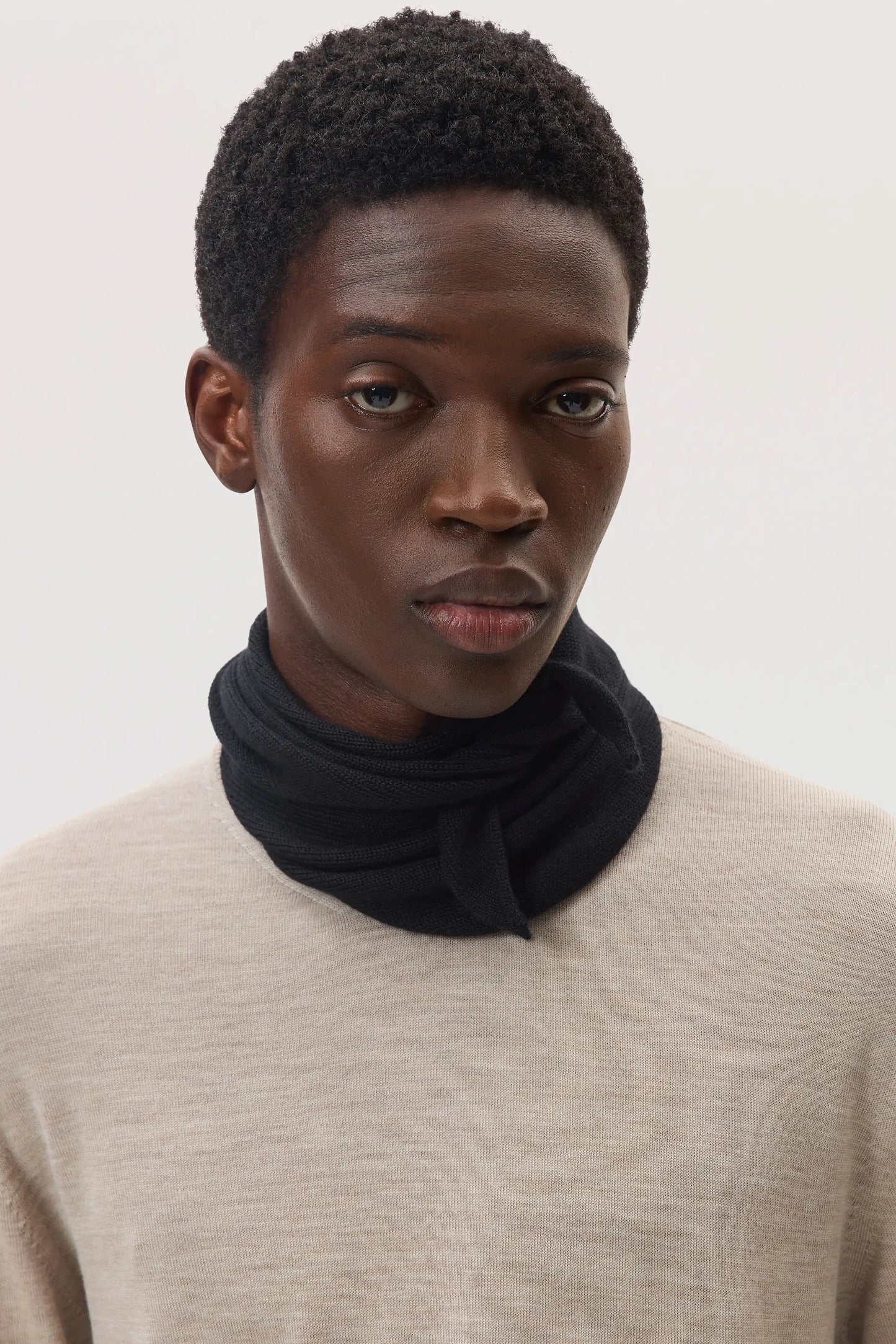 Male model wearing Johnstons of Elgin SS25 Accessories Black Triangle Cashmere Silk Neck Tie with a classic ash cashmere sweater, on a white background HBE03506SA0900ONE