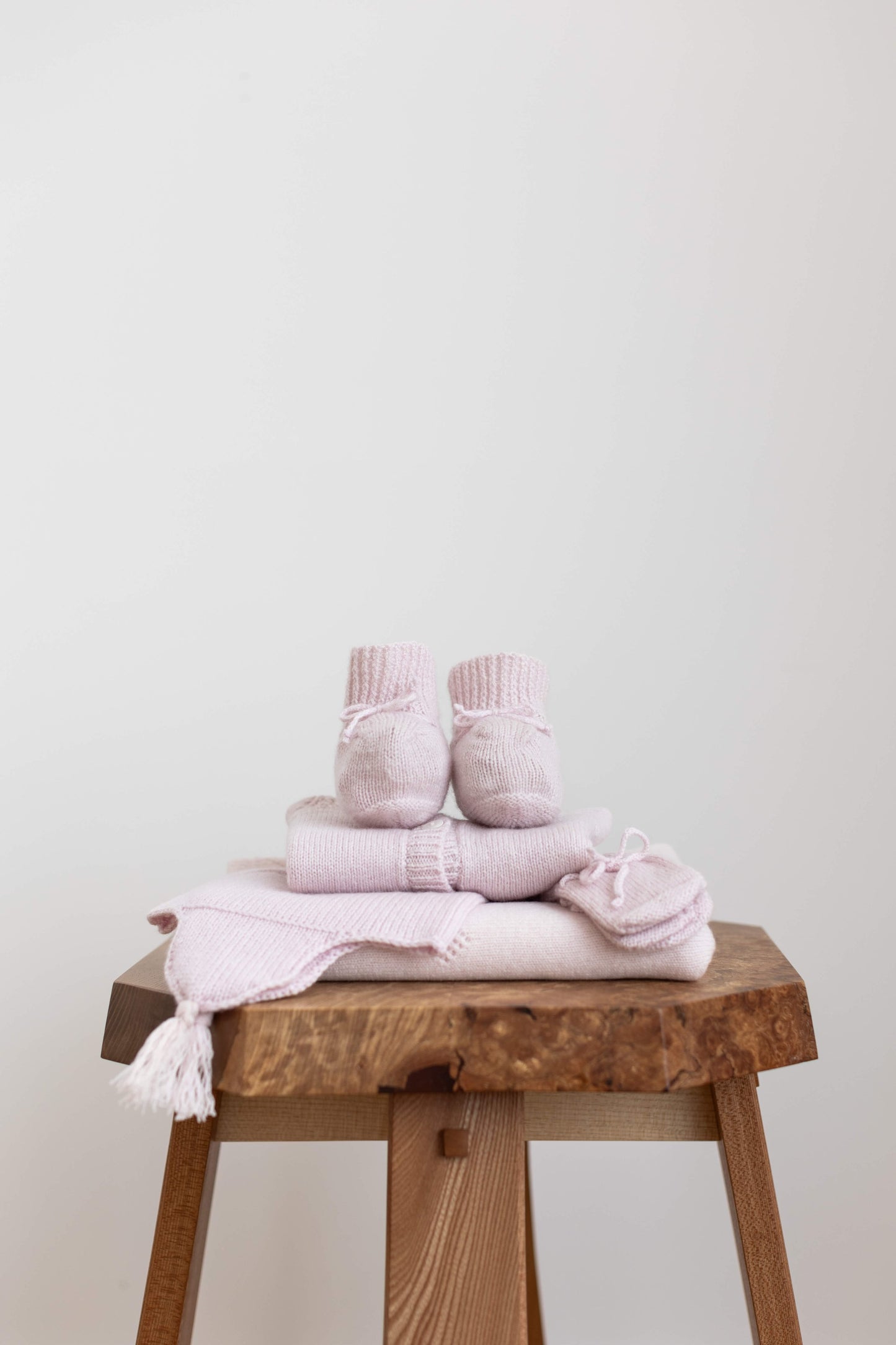 Johnstons of Elgin Hand Knitted Cashmere Baby Booties in Blush on pink check background JA000114SE0208ONE