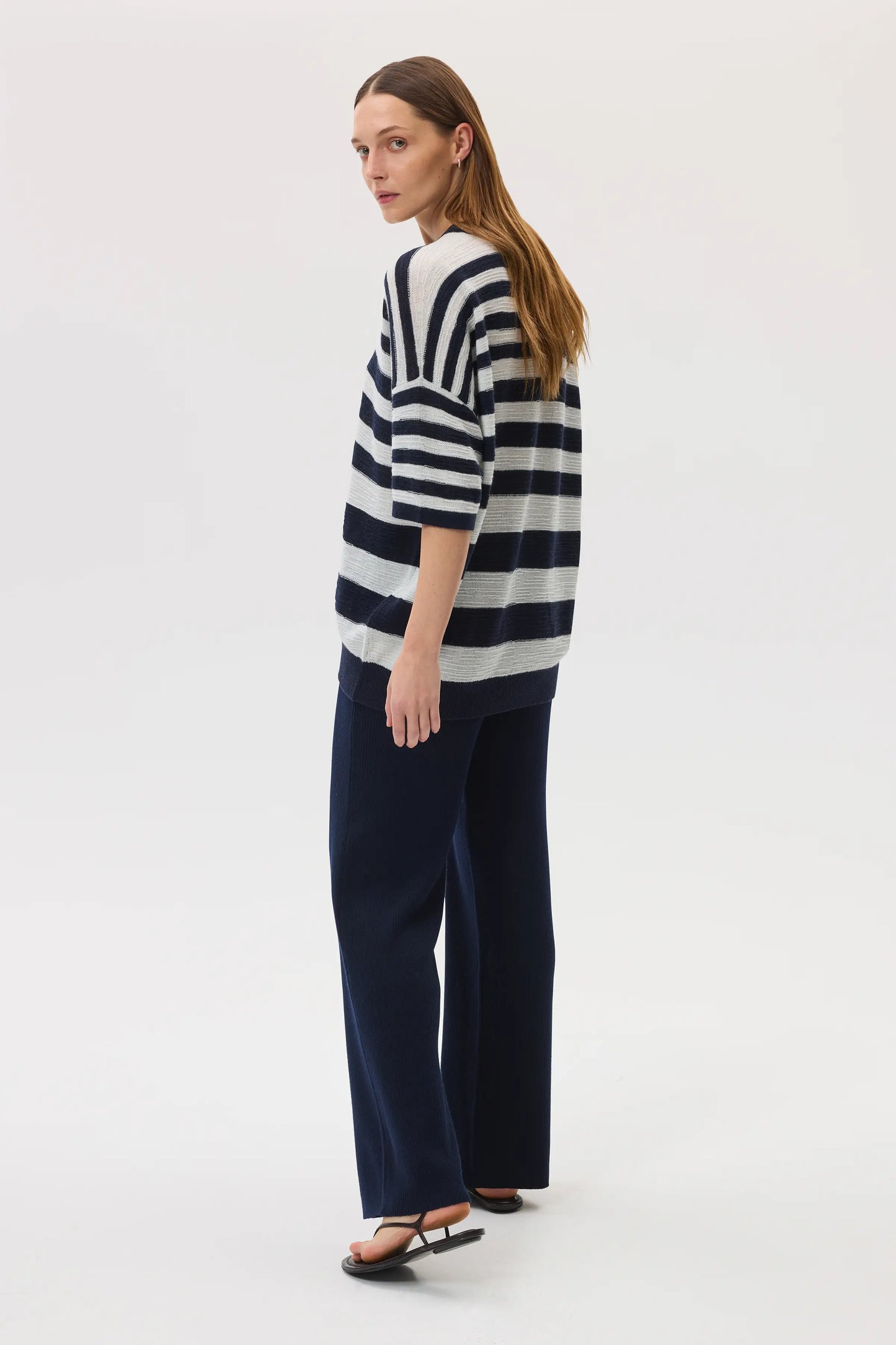 Female model wearing Johnstons of Elgin SS25 Unisex Knitwear Navy & White Textured Stripe Oversized Cashmere T-Shirt with navy trousers KAA05414Q25123