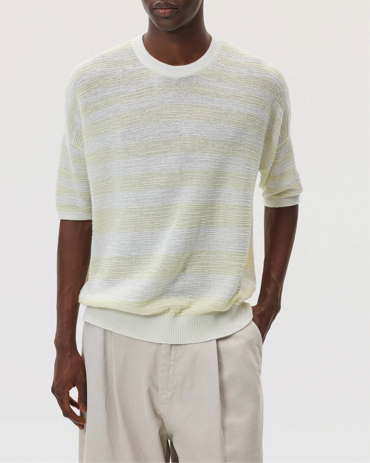 Male model wearing Johnstons of Elgin SS25 Unisex Knitwear White & Lemon Textured Stripe Oversized Cashmere T-Shirt with cream chino trousers against a white backdrop KAA05414Q25127