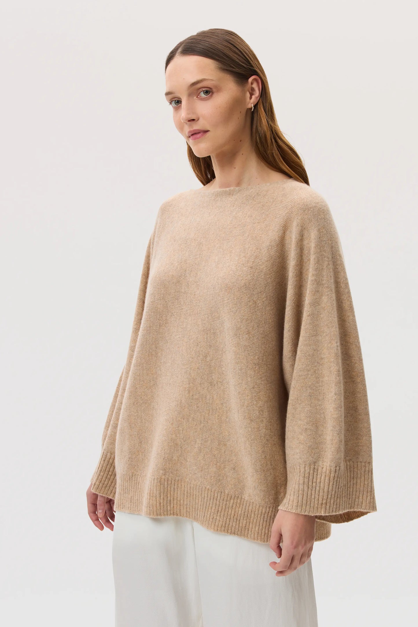 Model wearing Johnstons of Elgin SS25 Women's Knitwear Oatmeal Cashmere Cape Jumper with white trousers KAI05048HB0210