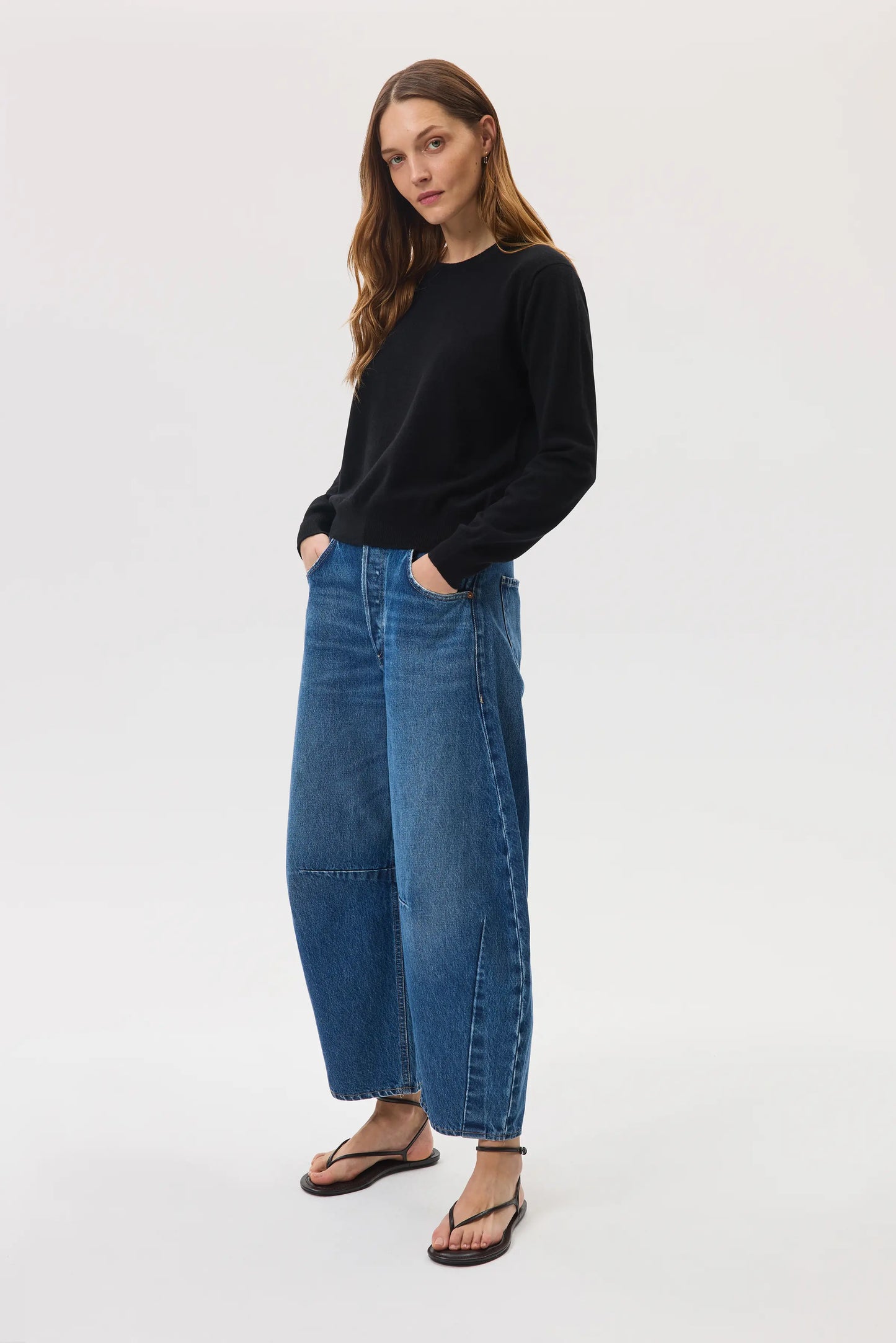 Model wearing Johnstons of Elgin SS25 Women's Knitwear Black Classic Cashmere Round Neck Sweater with blue barrel leg jeans on a white background KAI05142SA0900