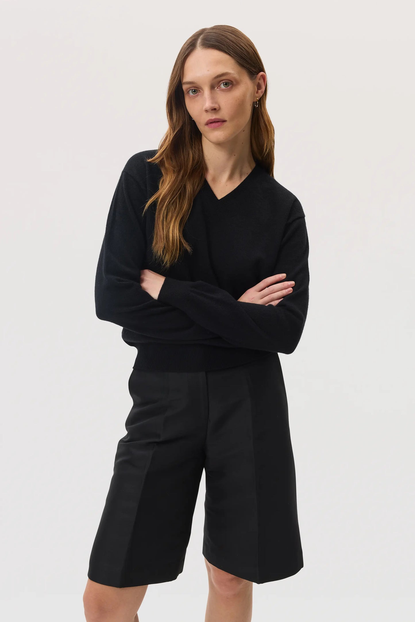 Model wears Johnstons of Elgin SS25 Women's Knitwear Black Classic Cashmere V Neck Jumper with black knee length shorts KAI05143SA0900