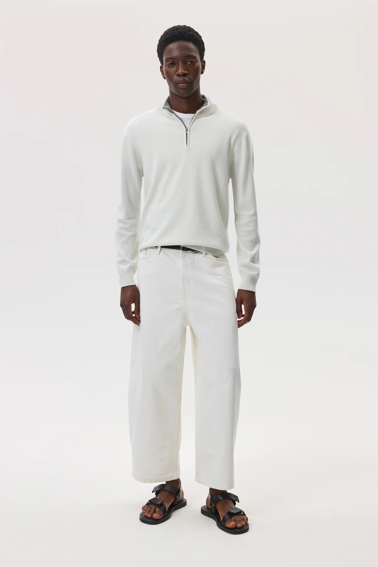 Model wearing Johnstons of Elgin SS25 Men's Knitwear White & Light Grey Contrast Trim Cashmere Zip Neck Jumper with white trousers on a white backdrop KAI05233Q25115