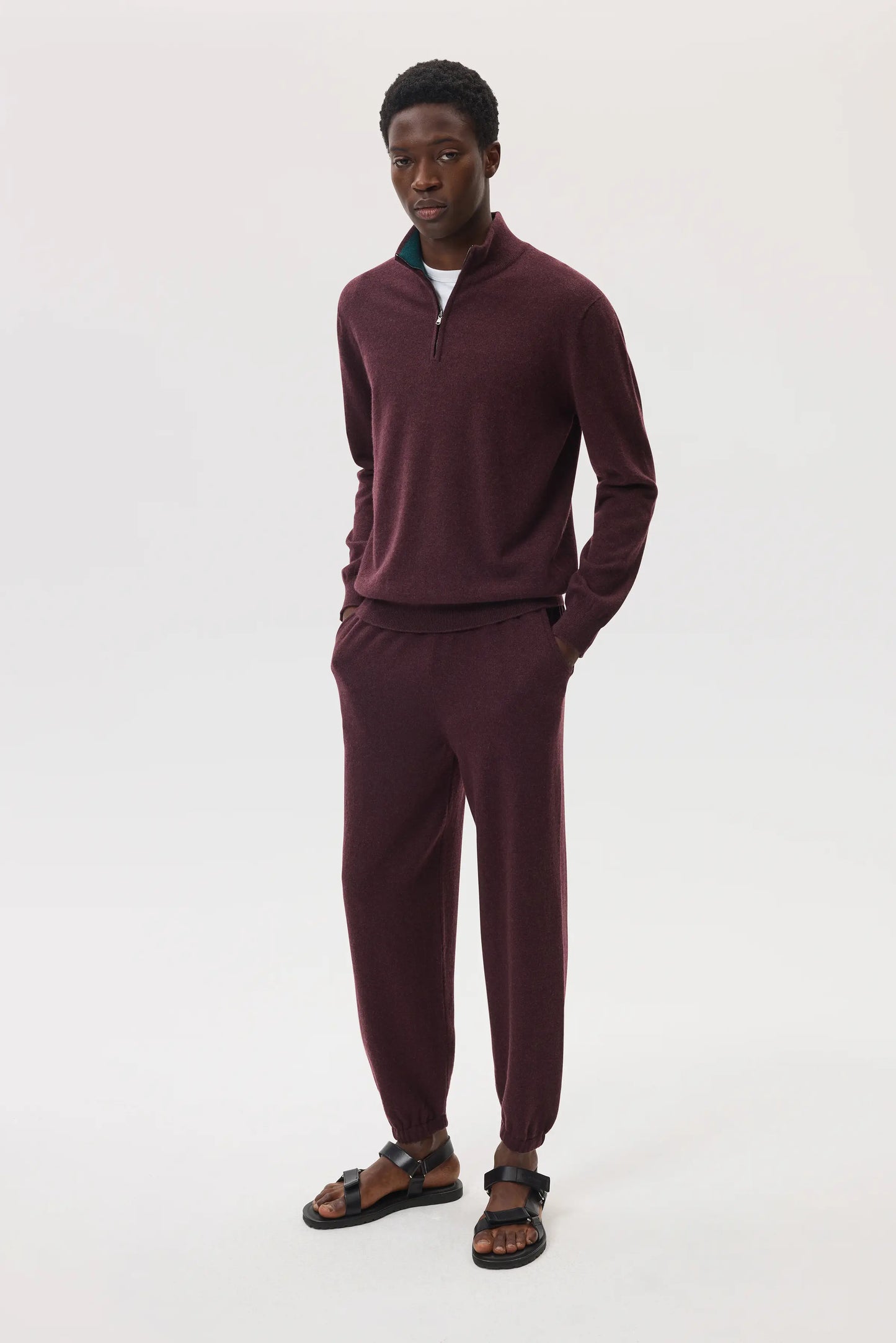 Model wearing Johnstons of Elgin SS25 Men's Knitwear Rosewood & Emerald Contrast Trim Cashmere Zip Neck Jumper over a white t-shirt, with cashmere joggers in rosewood KAI05233Q25116