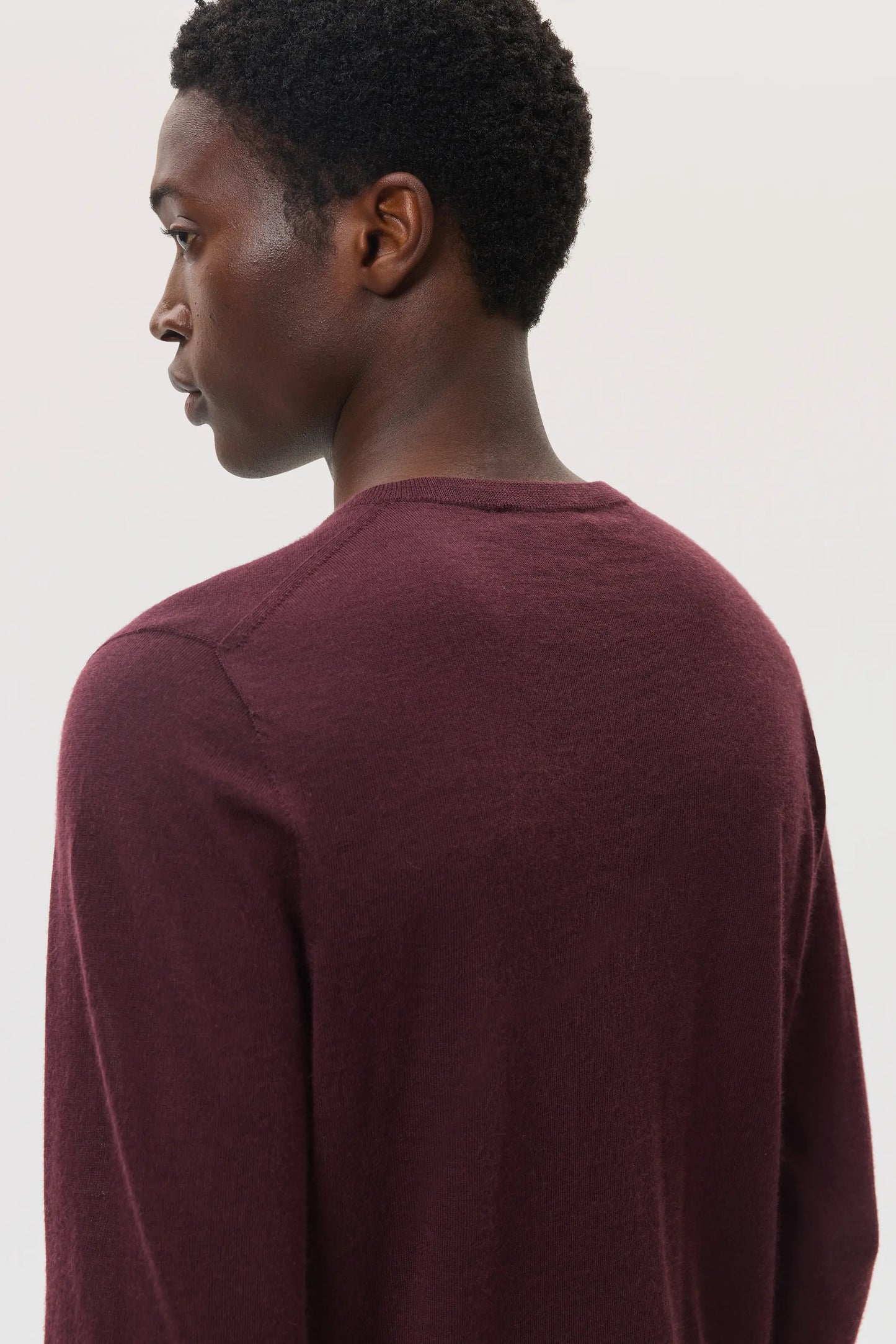 Male model wearing Johnstons of Elgin SS25 Unisex Knitwear Rosewood Superfine Cashmere V Neck Sweater on a white background KAI05242SB7255