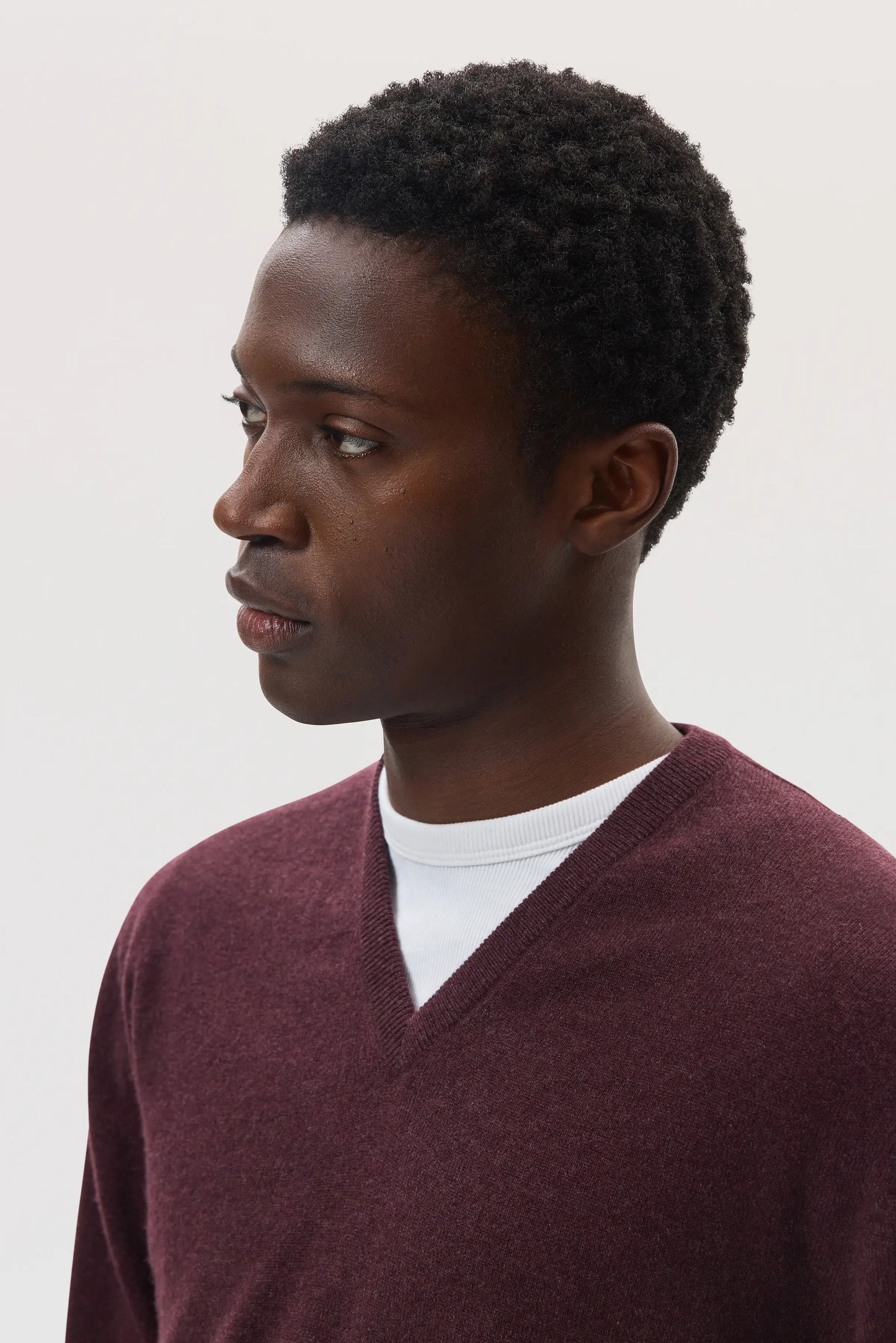 Model wearing Johnstons of Elgin SS25 Men's Knitwear Rosewood Classic Cashmere V Neck Jumper on a white background KAI05266SB7089