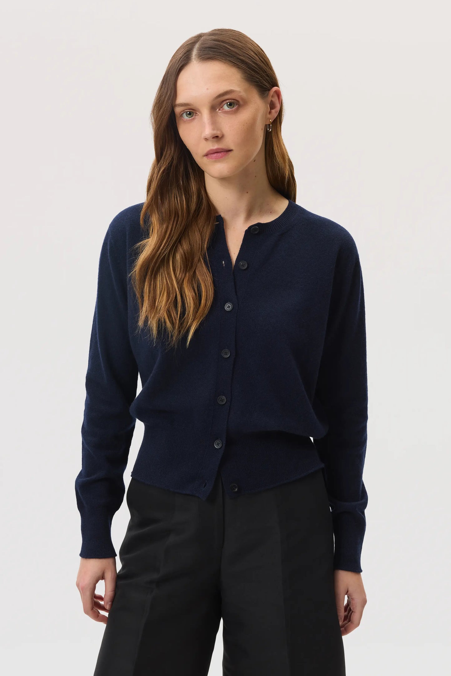 Model wears Johnstons of Elgin SS25 Women's Knitwear Navy Classic Cashmere Cardigan with navy shorts KAI05274SD7286