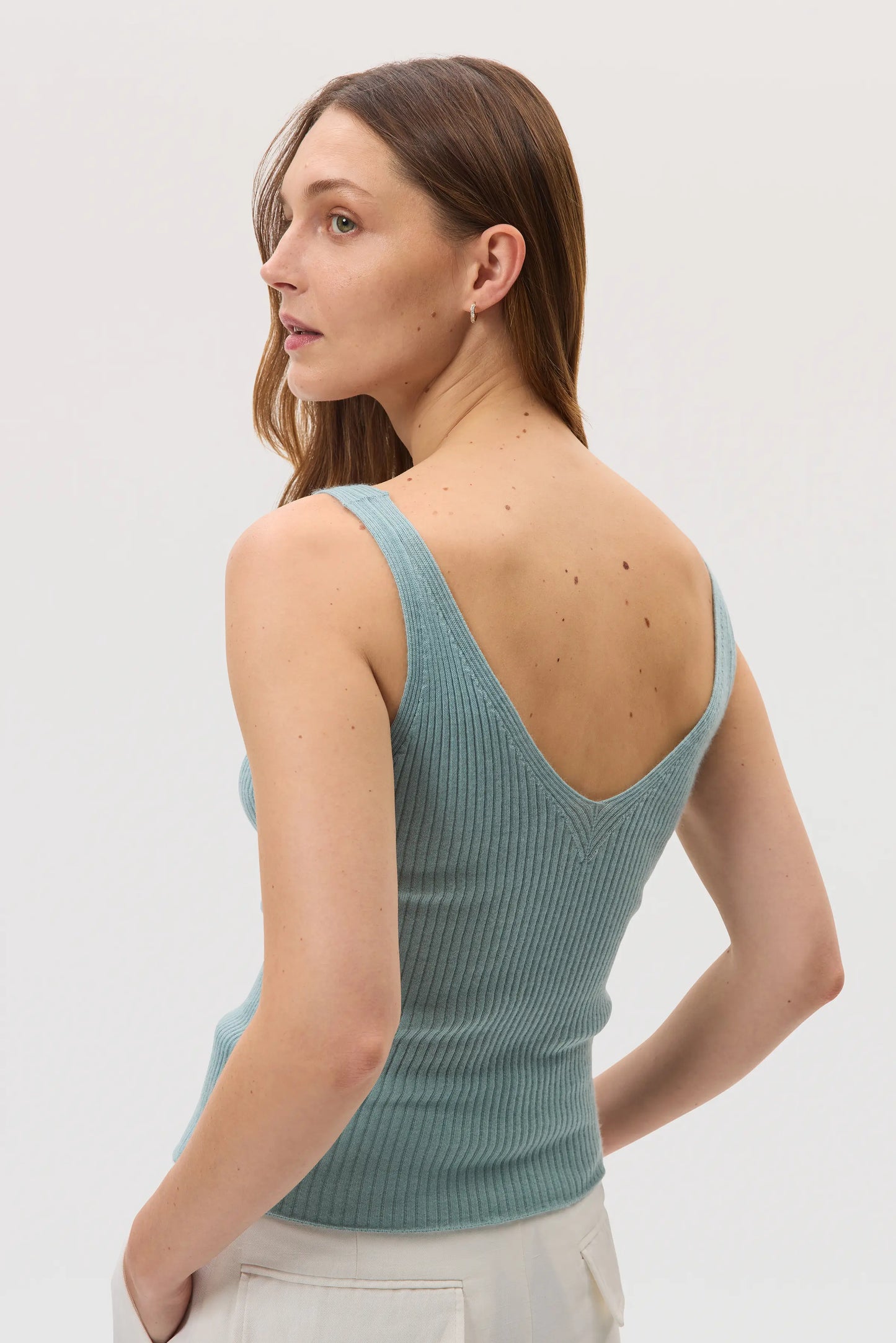 Model is wearing Johnstons of Elgin SS25 Women's Knitwear Sage Ribbed Superfine Cashmere Vest in a studio setting KAI05446SC0249