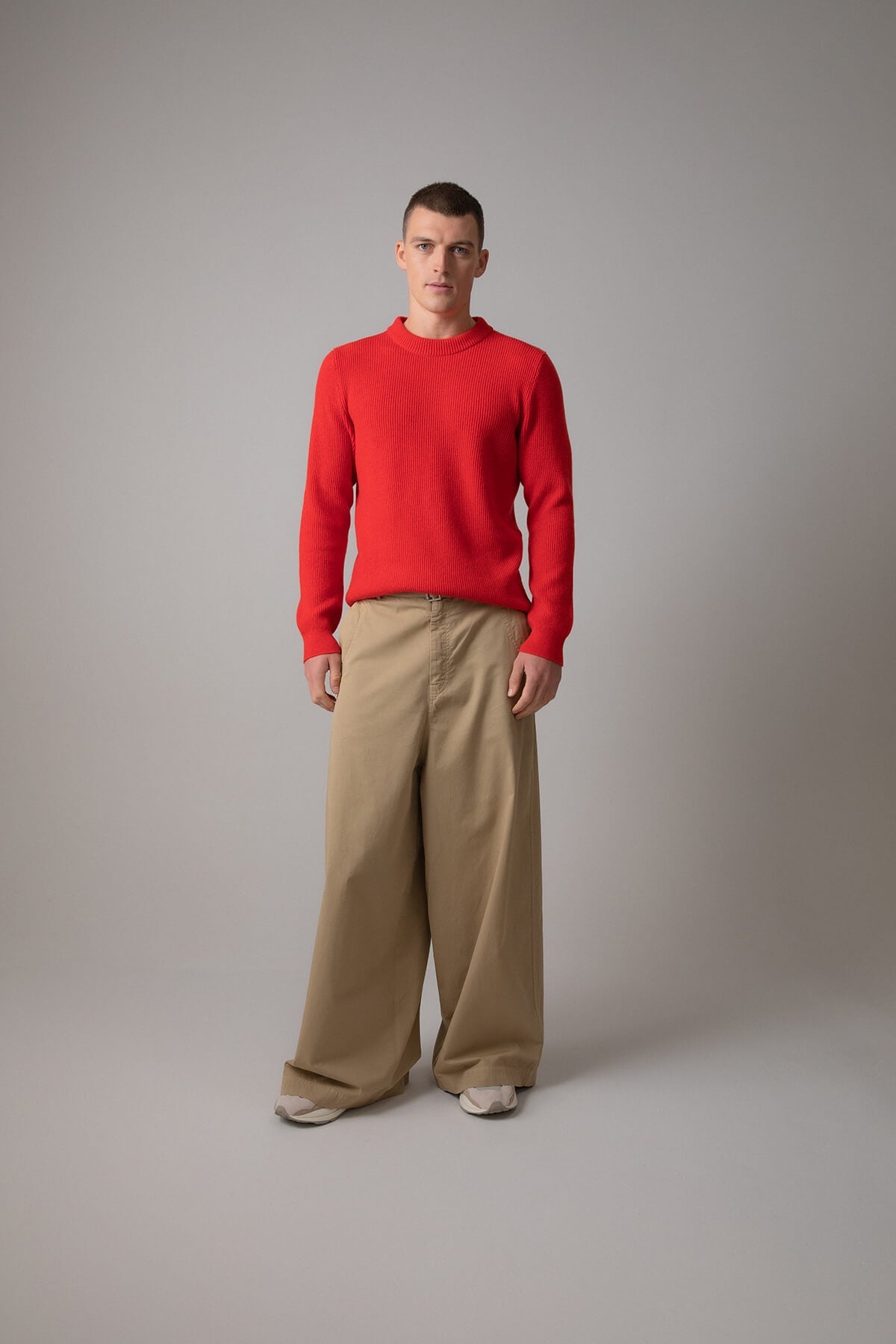 Johnstons of Elgin Men’s Ribbed Cashmere Round Neck Jumper in Orkney Red on model wearing camel trousers on grey background KAP05144SE0661