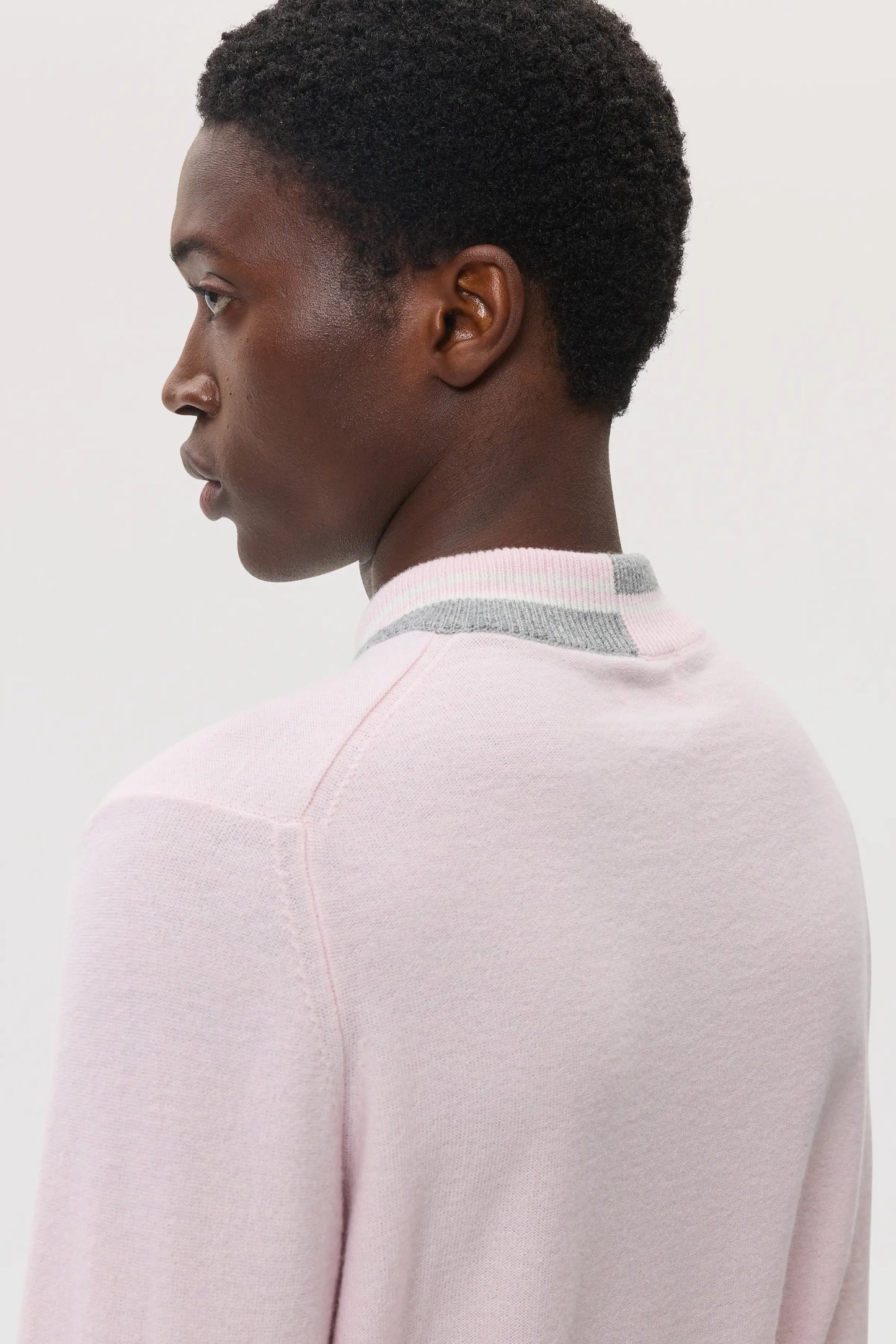 Model wearing Johnstons of Elgin SS25 Men's Knitwear Rose and grey Cashmere Vee Neck with Striped Trim Sweater on a white background KAP05410Q25121