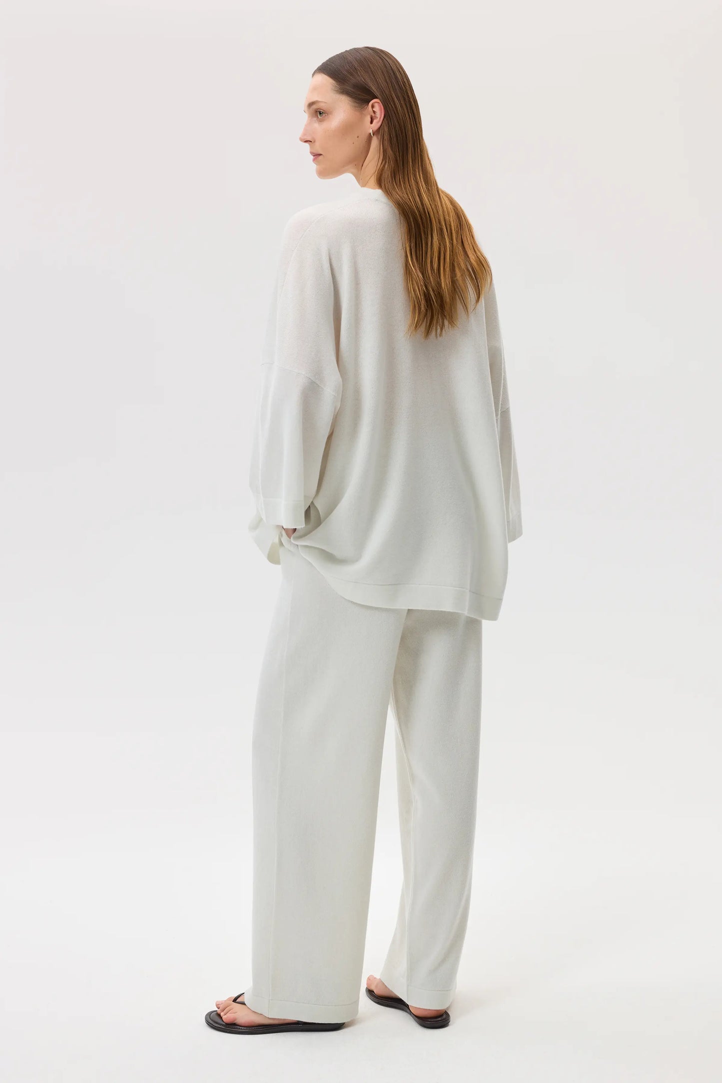 Model wears Johnstons of Elgin SS25 Women's Knitwear White Relaxed Featherlight Cashmere Jumper with white cashmere culottes and black sandals in a studio setting KAP05426HA0346