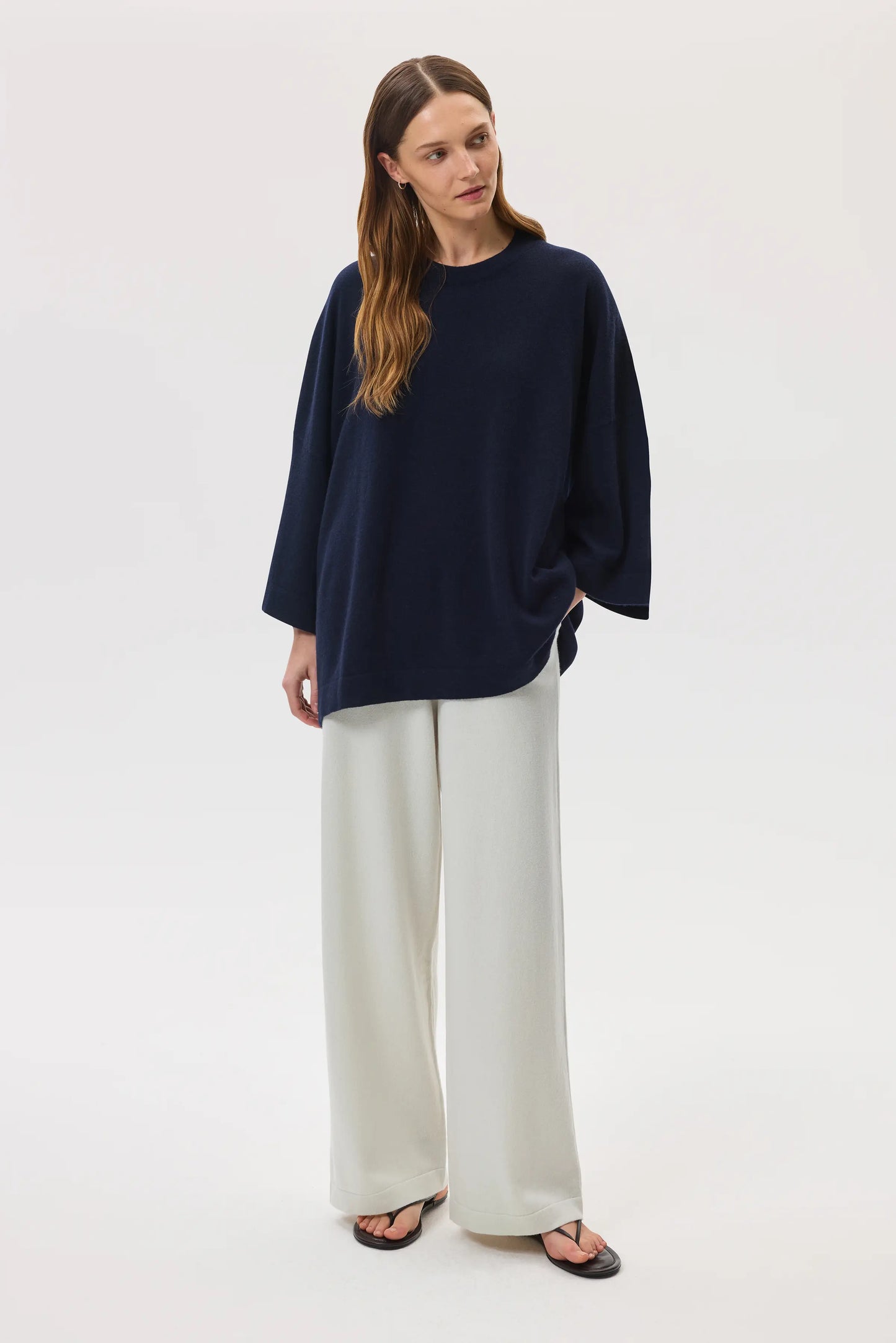 Model wears Johnstons of Elgin SS25 Women's Knitwear Navy Relaxed Featherlight Cashmere Jumper with white trousers and black sandals KAP05426SD7286