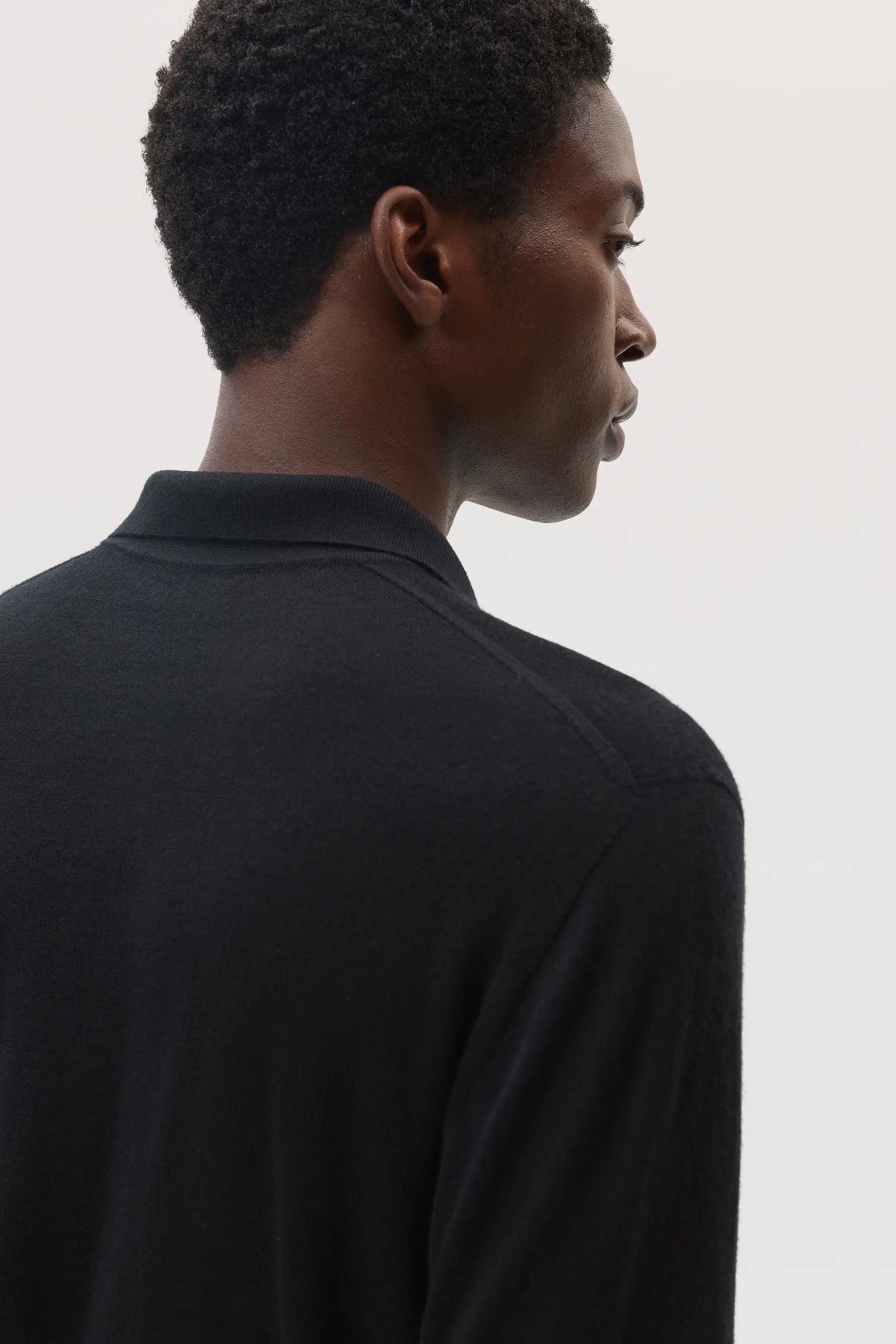 Model wears Johnstons of Elgin SS25 Men's Knitwear Black Superfine Cashmere Silk Polo shirt on a studio backdrop KBI00964SA0900