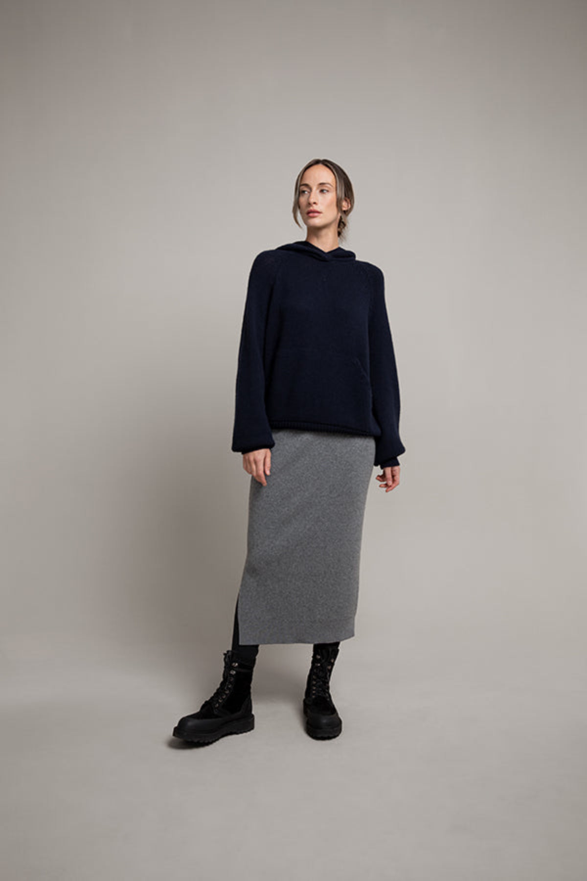 Person wearing a navy sweater and gray skirt against a plain background KBP00923HA5931