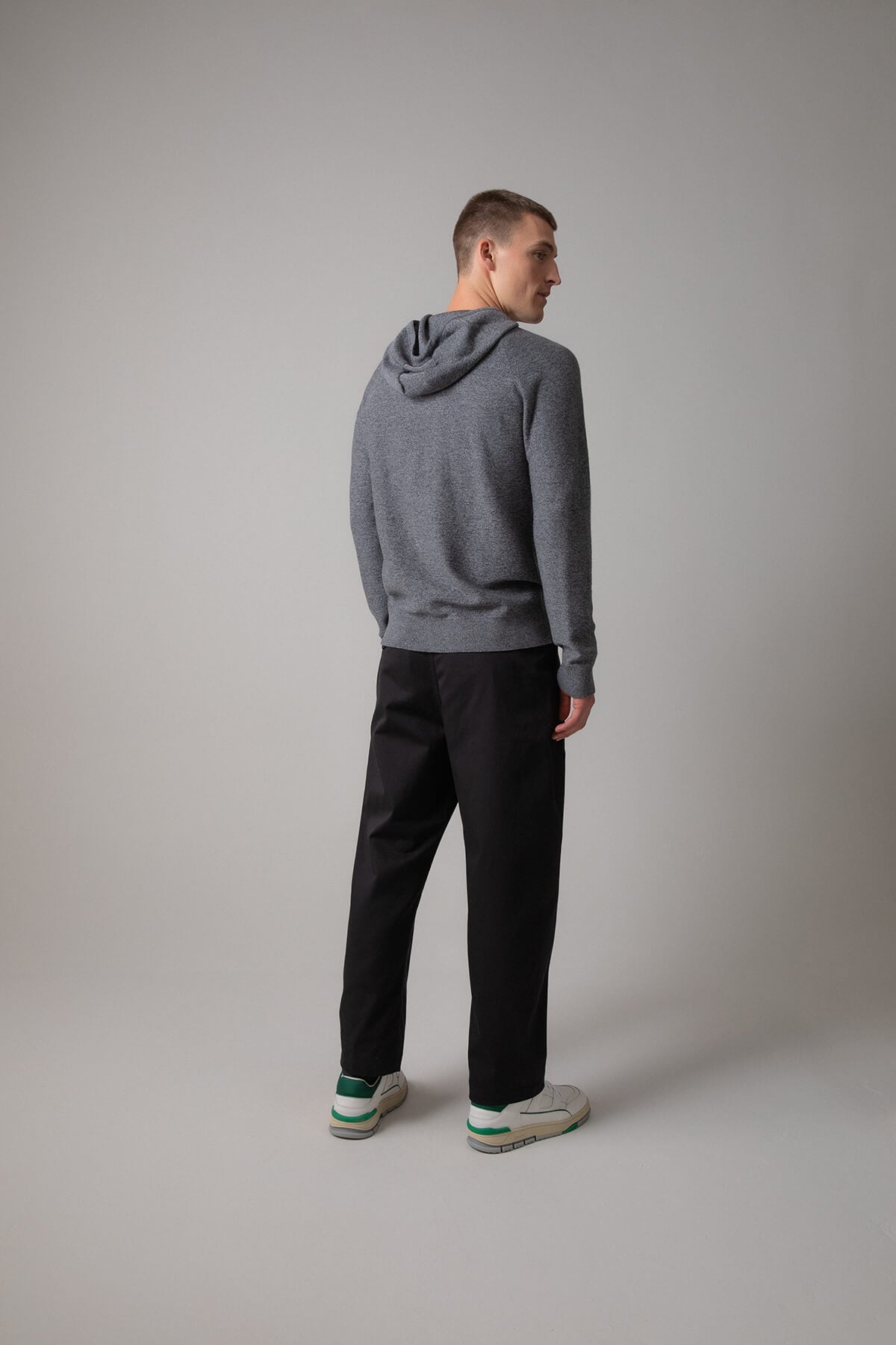 Johnstons of Elgin’s Men's Seamless Merino Hoodie in Granite grey on model wearing black trousers on a grey background KDI00665HA7160