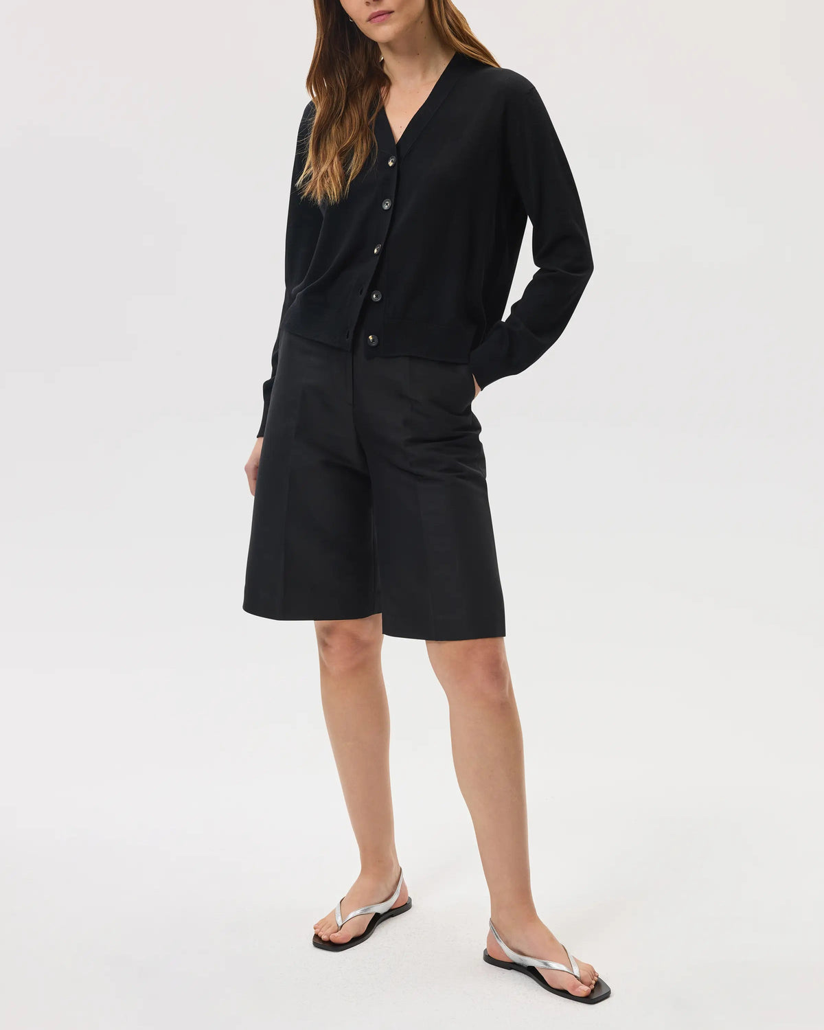 Model wearing Johnstons of Elgin SS25 Women's Knitwear Black Superfine Merino Wool Cardigan with black shorts against a white background KDI00686SA7131