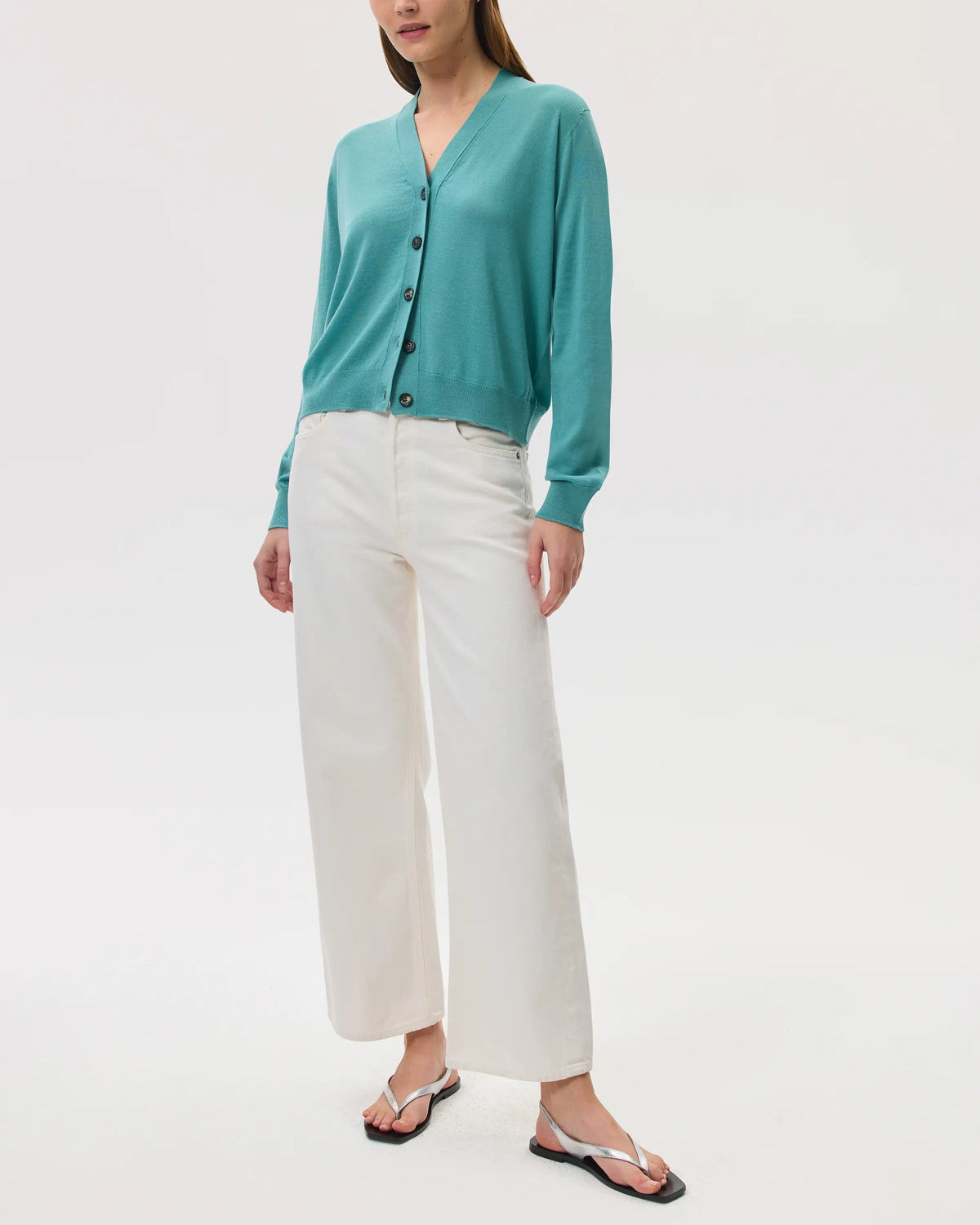 Model wears Johnstons of Elgin SS25 Women's Knitwear Jade Superfine Merino Wool Cardigan with white trousers and silver sandals KDI00686SC4641