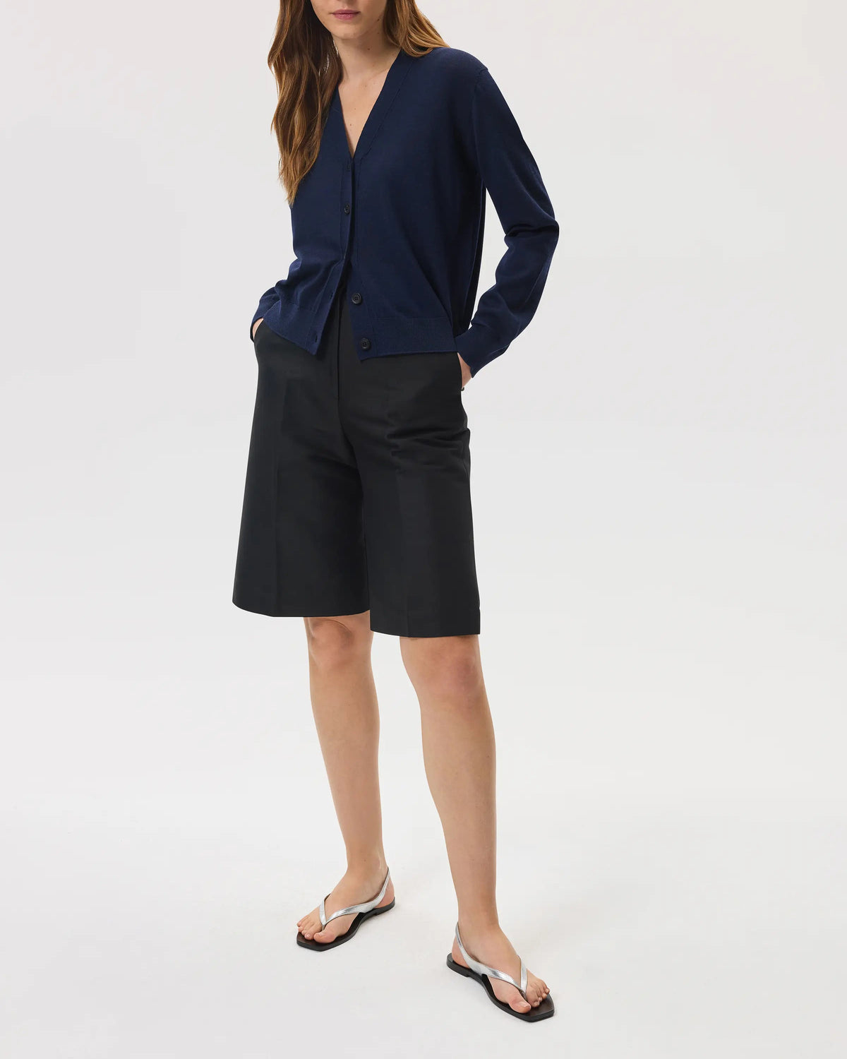 Model wears Johnstons of Elgin SS25 Women's Knitwear Navy Superfine Merino Wool Cardigan with black shorts on a white background KDI00686SD7563
