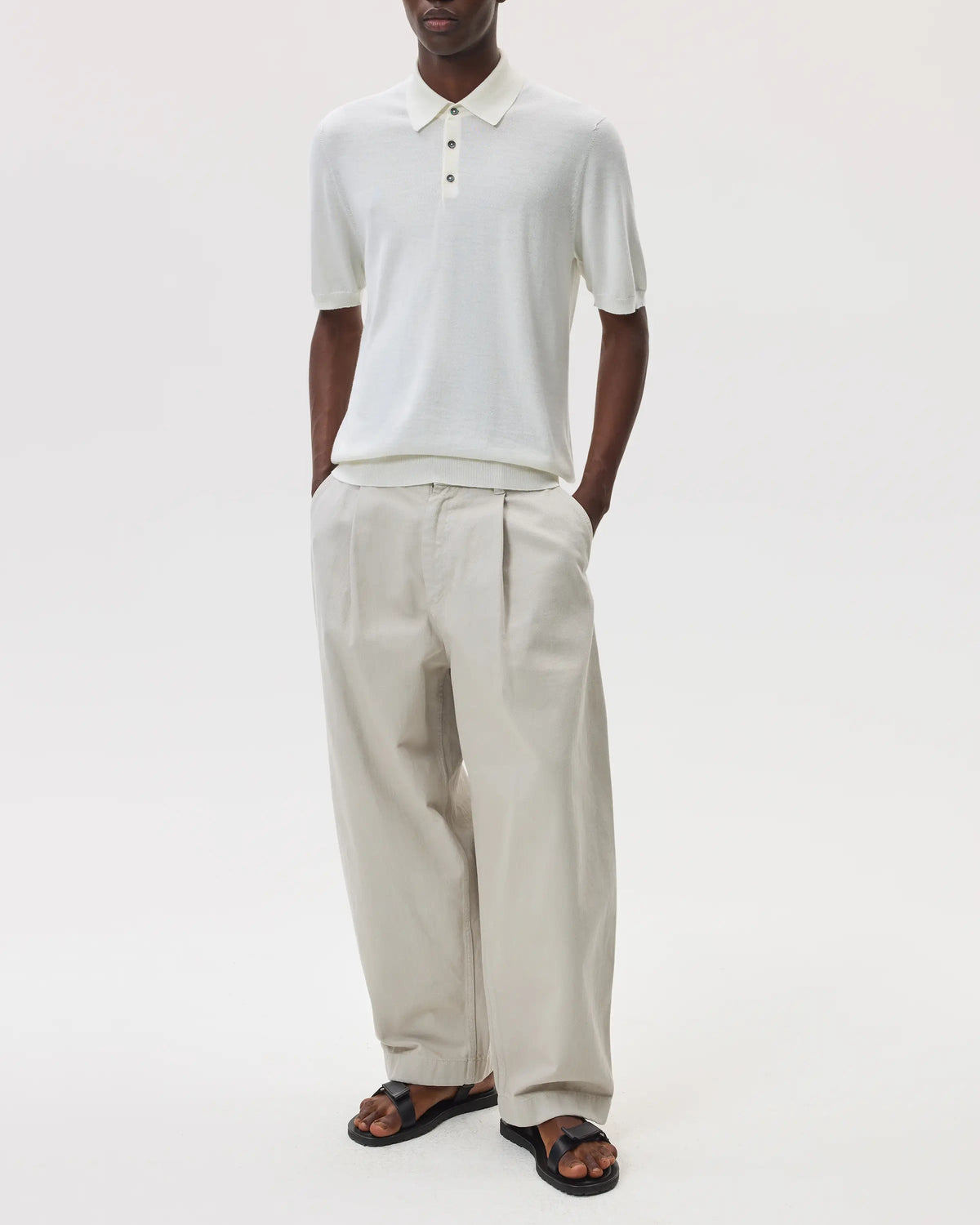 Male model wearing Johnstons of Elgin SS25 Men's Knitwear White Superfine Merino Polo Shirt with beige chinos on a white backdrop KDI00715SA0396