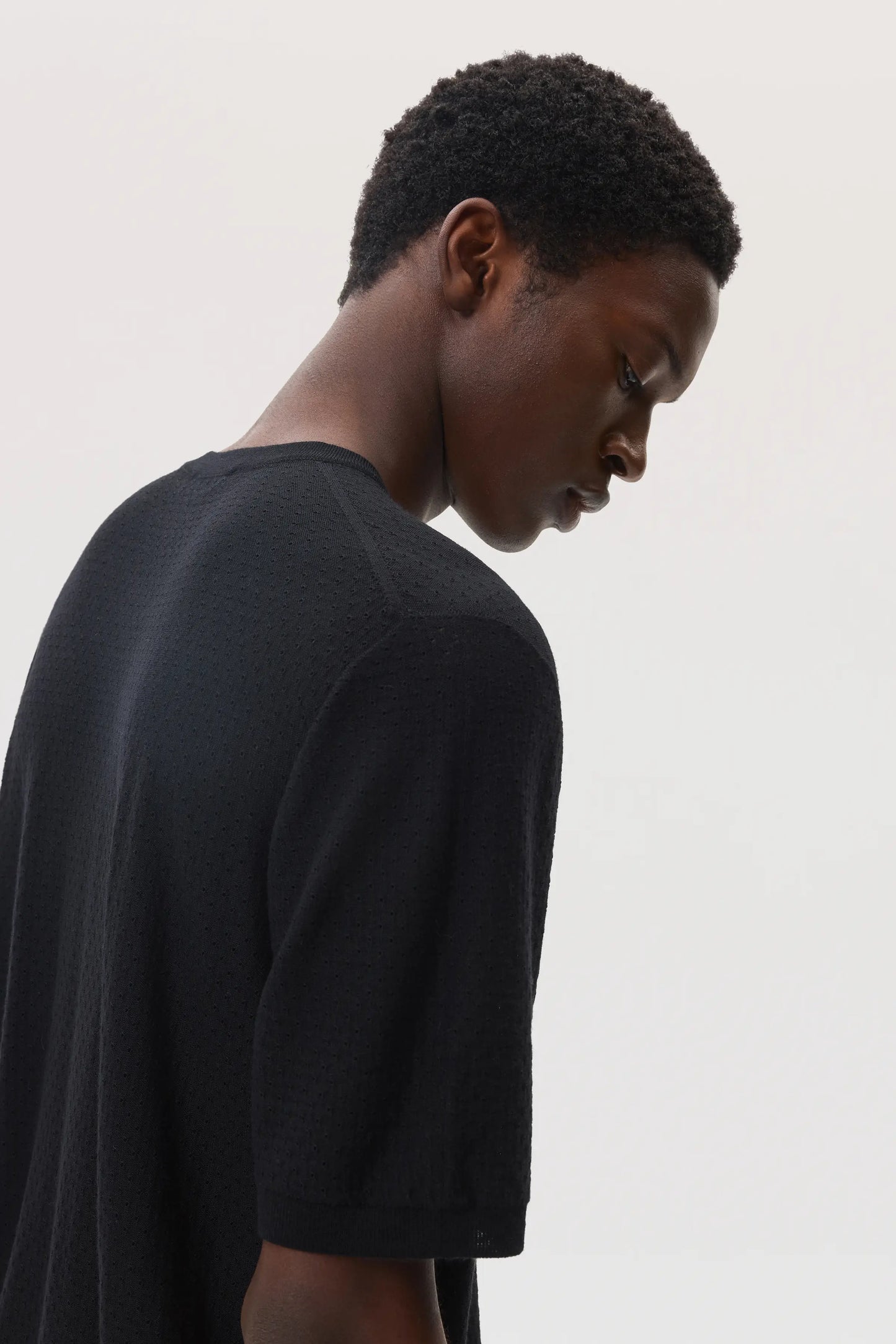 Model wearing Johnstons of Elgin SS25 Men's Knitwear Black Superfine Merino Mesh T-Shirt on a white background KDI00730SA7131