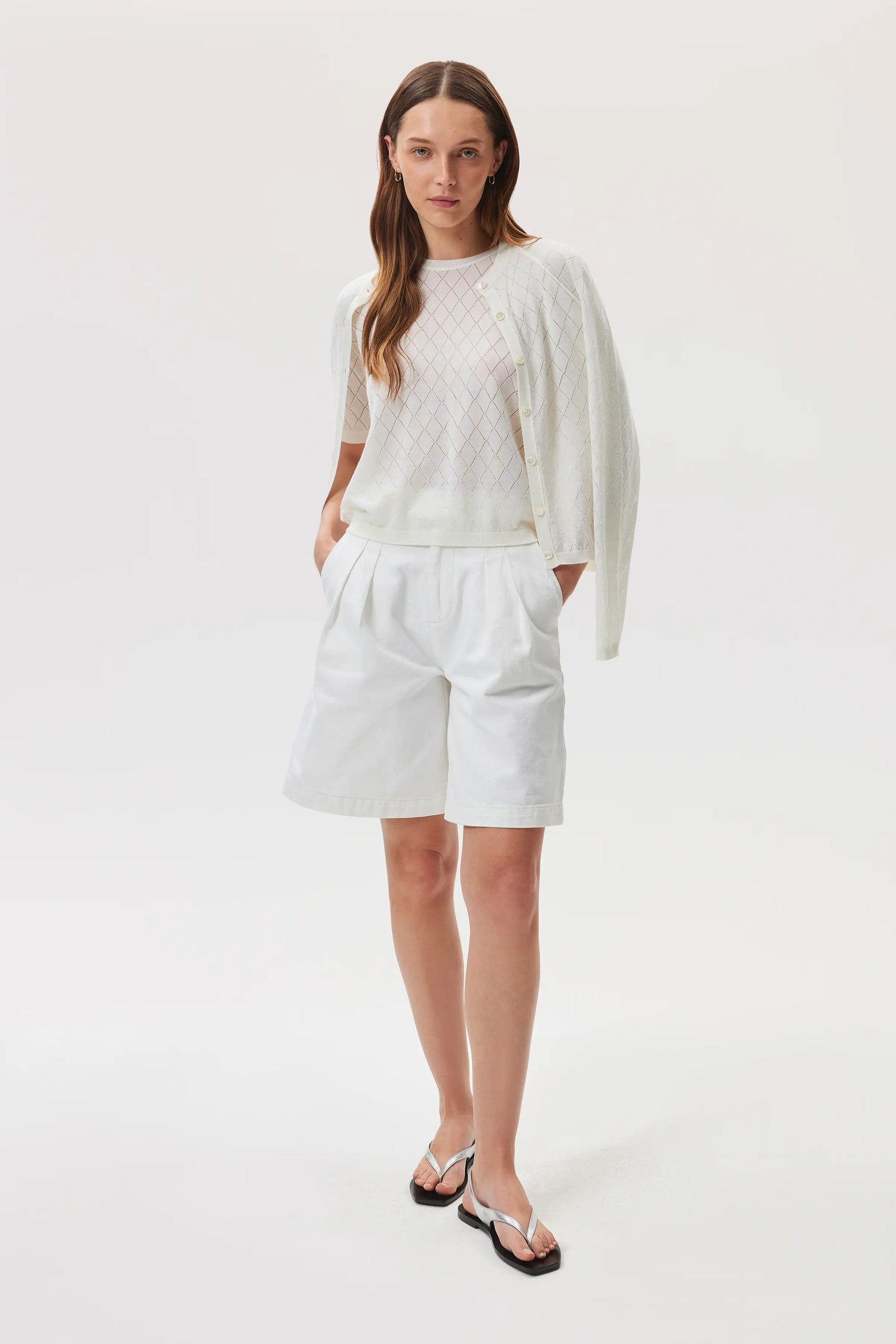 Johnstons of Elgin SS25 Women's Knitwear White Superfine Merino Pointelle Argyle T-Shirt and matching pointelle merino cardigan styled with white linen shorts in a studio setting KDI00739SA0396