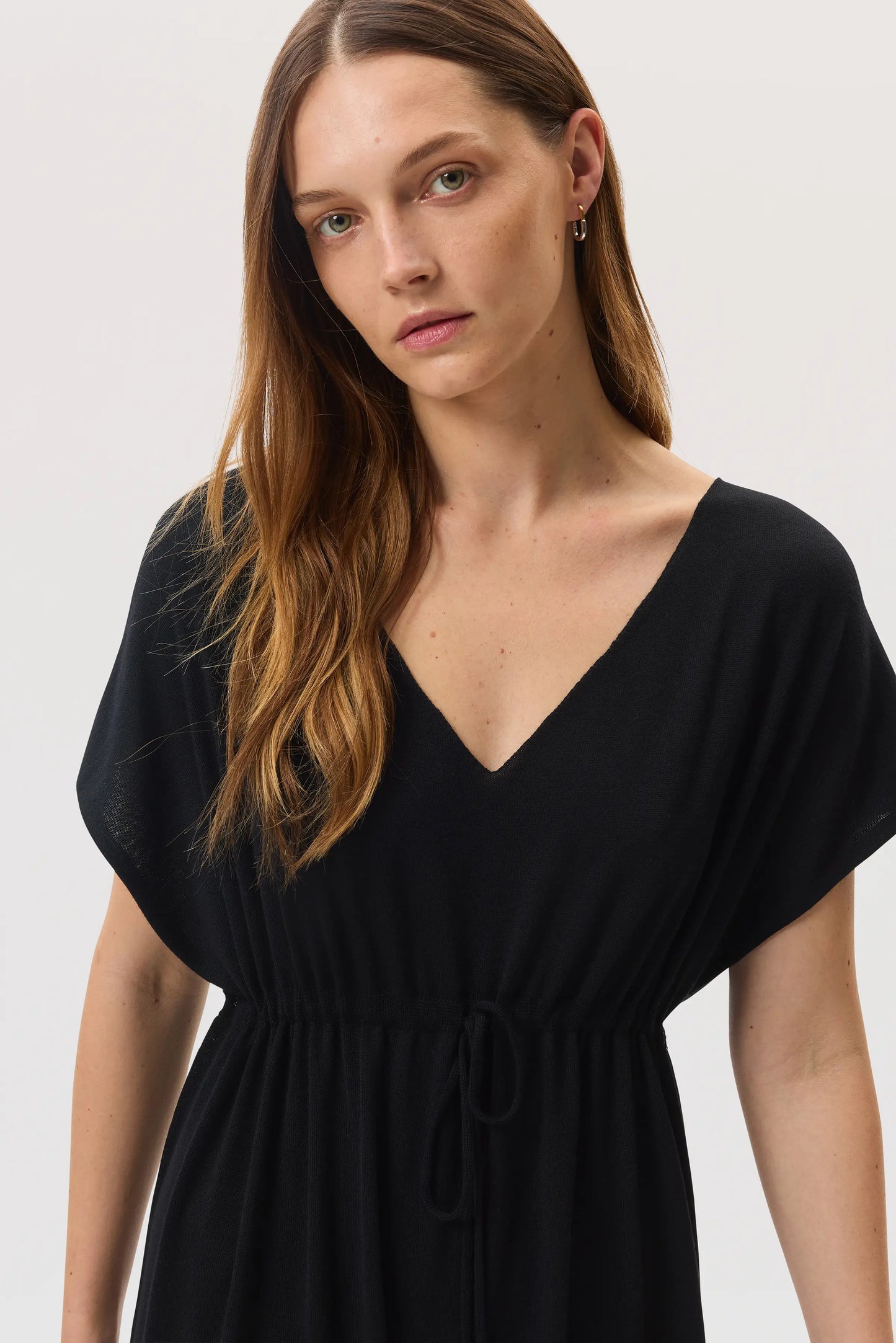 Model wears Johnstons of Elgin SS25 Women's Knitwear Black Superfine Merino Maxi Dress image shows the deep v neck style close up on a white backdrop KDI00744SA7131
