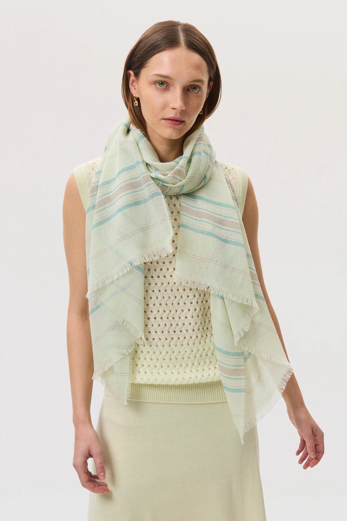 Female model wearing Johnstons of Elgin SS25 Accessories Green Lightweight Stripy Cashmere Scarf draped over a lemon yellow mesh cashmere tank top WA000861RU7593ONE