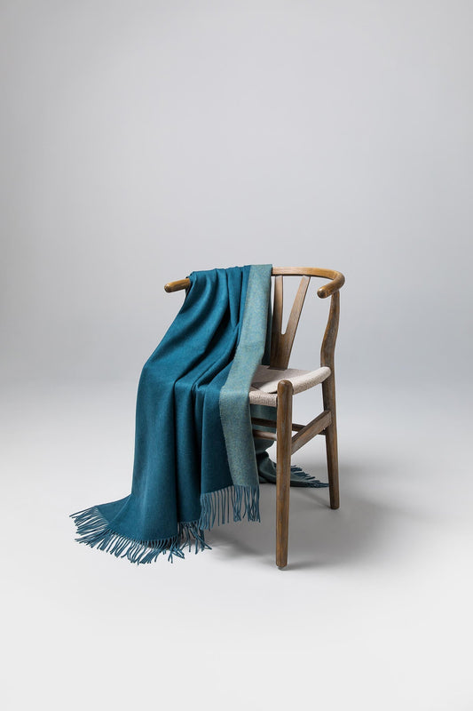 Johnstons of Elgin Reversible Pure Cashmere Throw in Teal & Lovat draped over a wooden chair on a white background WA000013RU7257ONE