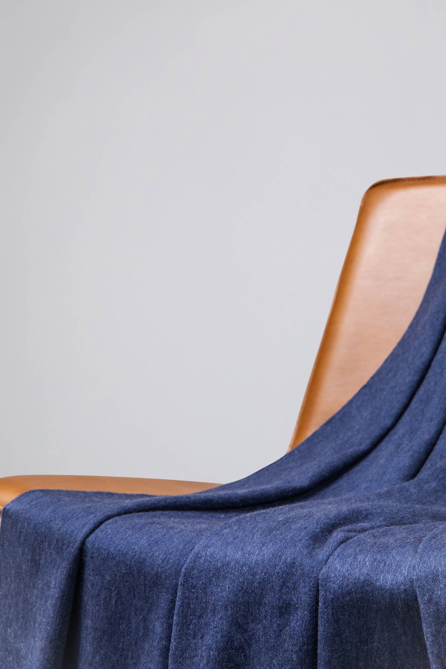 Johnstons of Elgin’s Denim Blue Cashmere Throw on brown chair on a grey background WA000055HD0724
