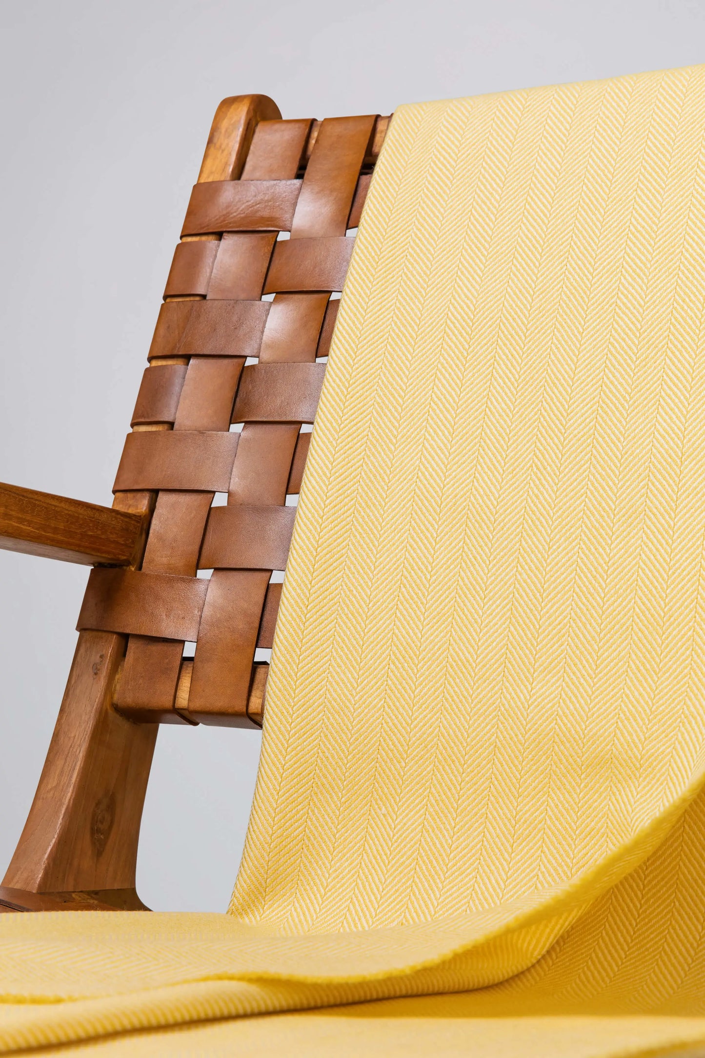 Johnstons of Elgin's Buttercup & White Herringbone Merino Throw on brown chair on a grey background WD000010RU7265ONE