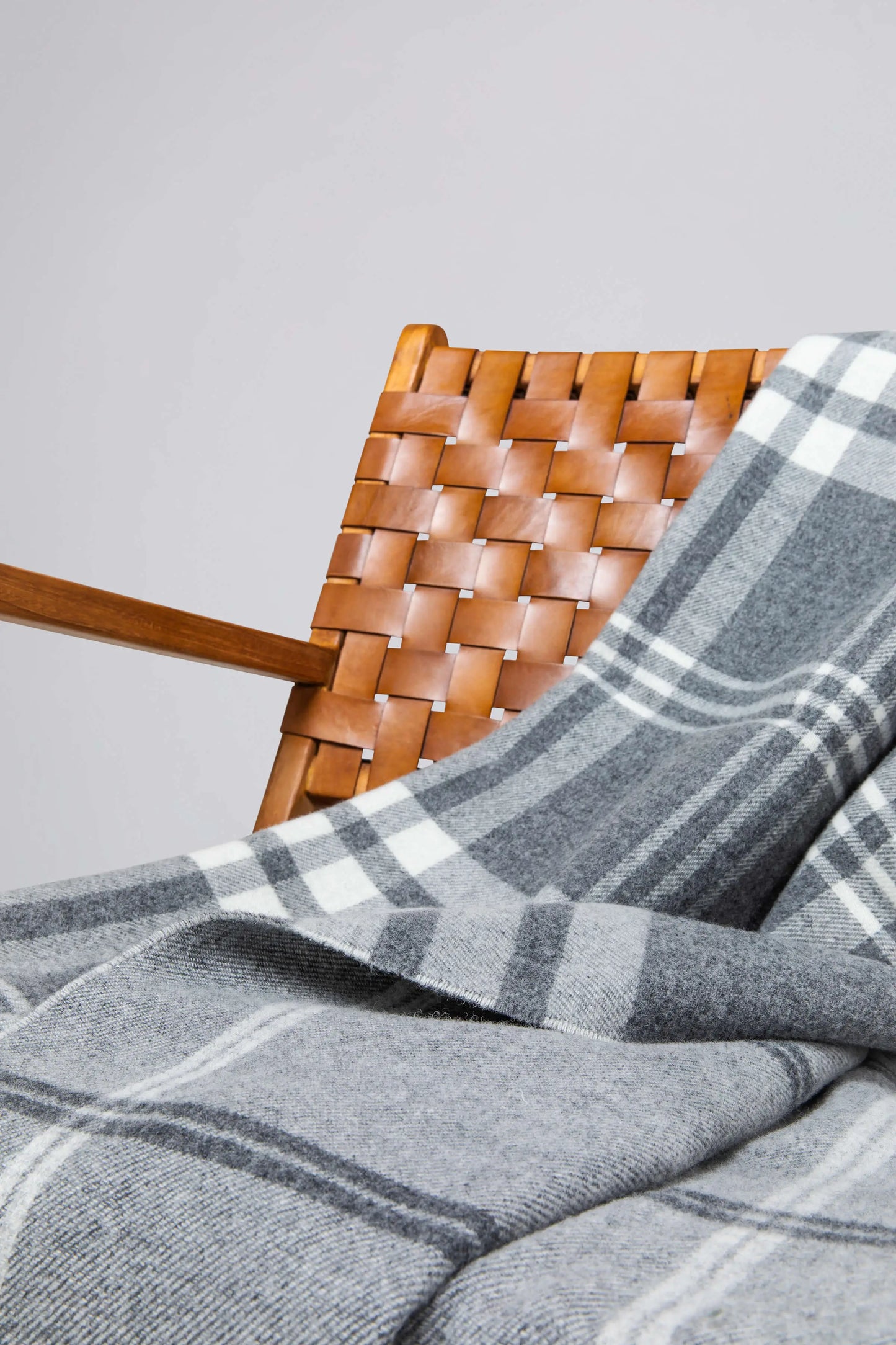 Johnstons of Elgin’s Double Face Grey & White Box Check Lambswool Throw on brown chair on a grey background WD000021RU6951ONE