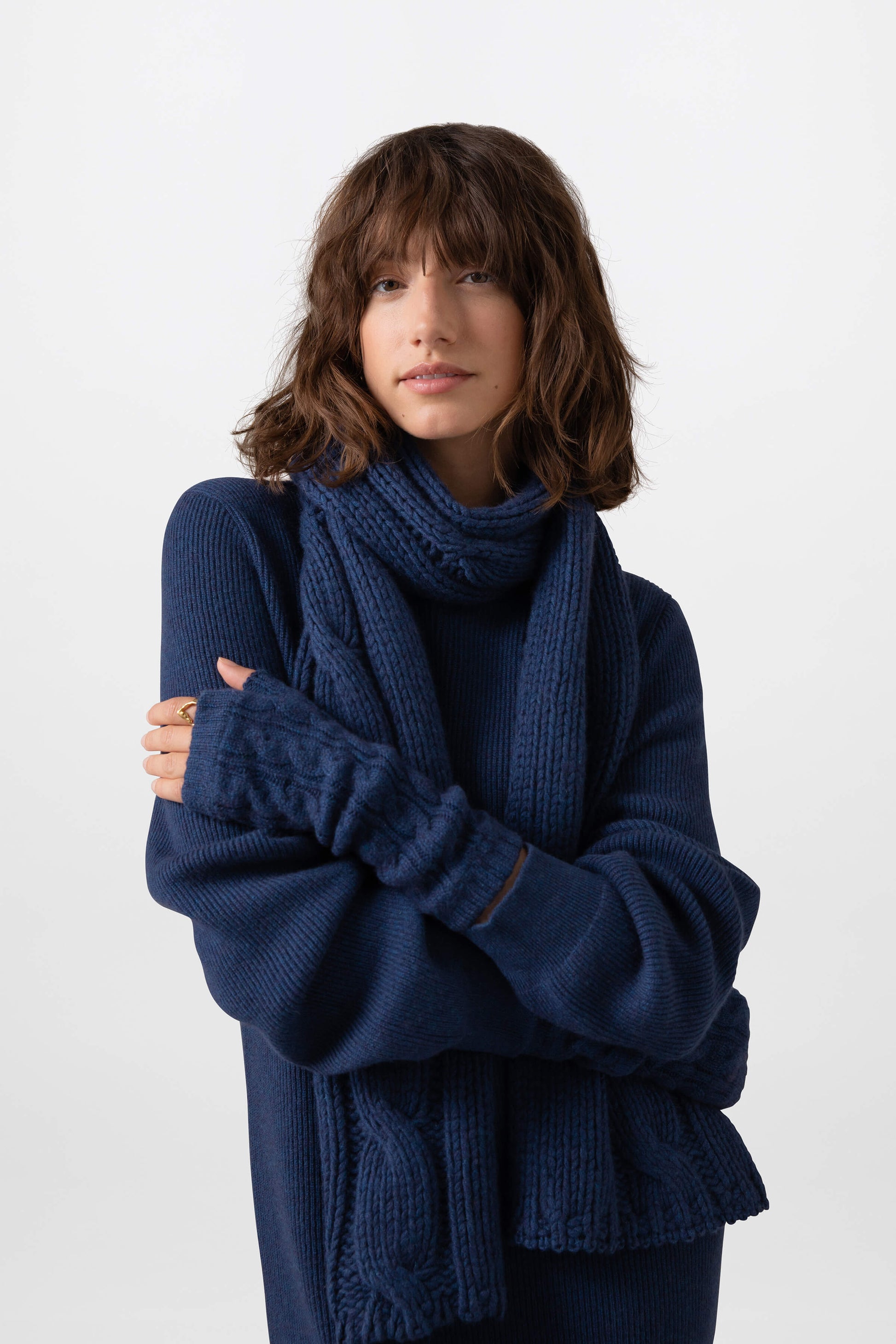Johnstons of Elgin’s Ocean blue Luxe Chunky Cable Cashmere Scarf on model wearing matching cashmere wrist warmers and blue cashmere jumper on a grey background HAB03195HD7244