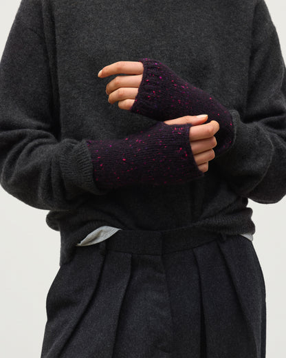 Close-up of a person wearing dark charcoal knit sweater and pleated dark trousers, with both hands adjusting a pair of fingerless knit wrist warmers in deep purple with pink flecks. PURPLE 100% CASHMERE HAC03644HD7360ONE