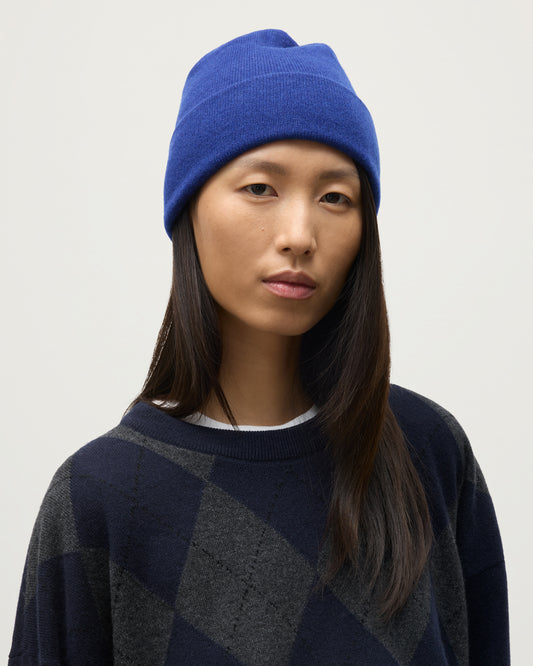 JOHNSTONS OF ELGIN BRAEMAR BEANIE BLUE 100% CASHMERE ON A FEMALE MODEL WITH DARK NAVY CLAN CASHMERE ARGYLL SWEATER HAE02655SD5326ONE