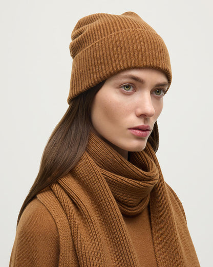 Female model wearing Johnstons of Elgin AW25 Knitted Accessories Dark Camel Slouchy Cashmere Beanie HAE03325SB4620ONE