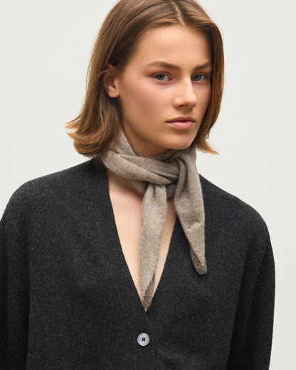 A woman with shoulder-length brown hair wearing a dark charcoal gray cardigan and a light taupe knit scarf, photographed against a clean off-white background. JOHNSTONS OF ELGIN CASHMERE GAUZY ANYA DIAMOND NECK TIE BROWN 100% CASHMERE HAE03431Q26241ONE