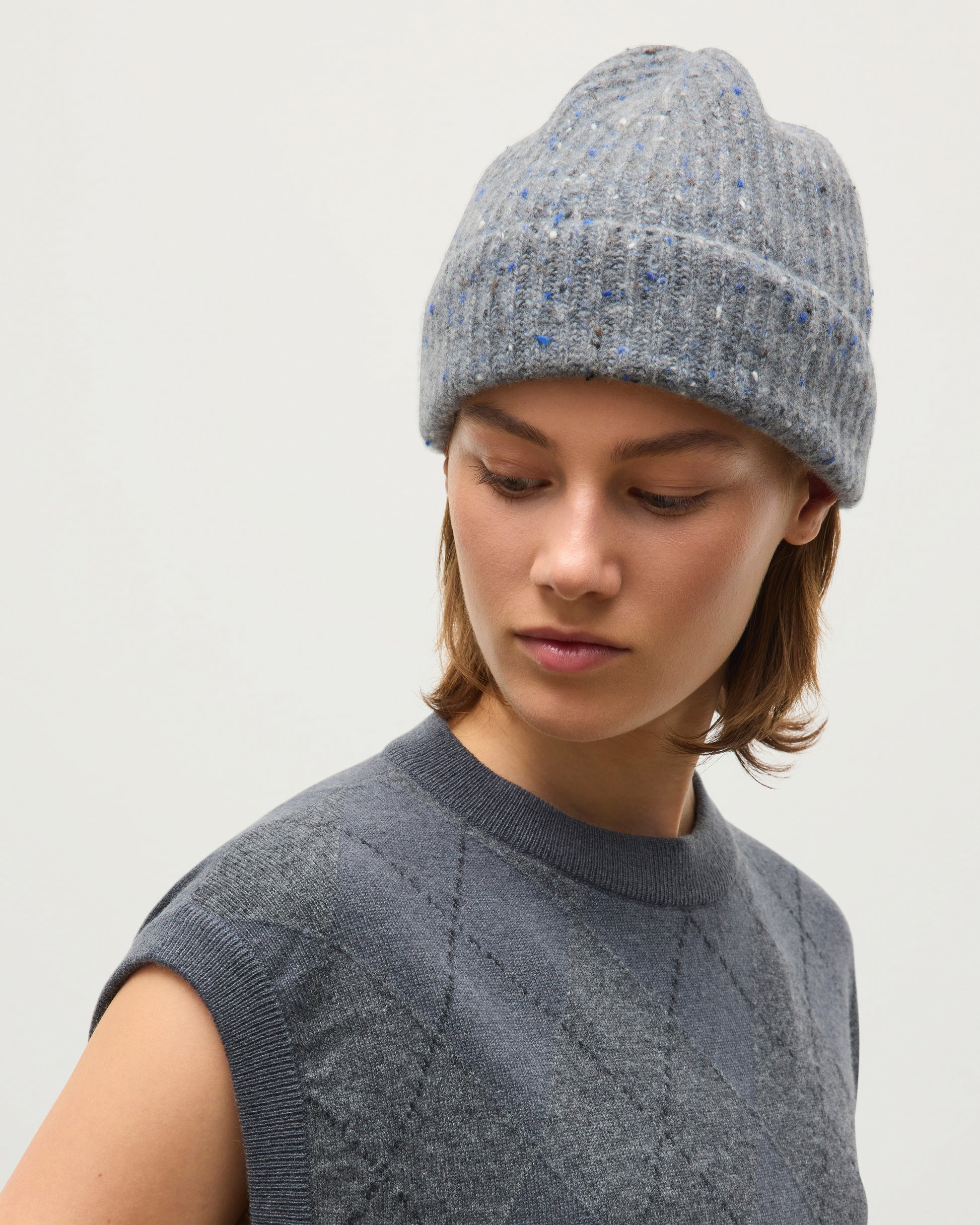 A woman wearing a gray ribbed knit beanie with subtle blue flecks and a matching gray knit sweater, photographed against a plain light gray background. JOHNSTONS OF ELGIN CASHMERE DONEGAL TRAQUAIR RIBBED BEANIE GREY 100% CASHMERE HAE03643HA4270ONE