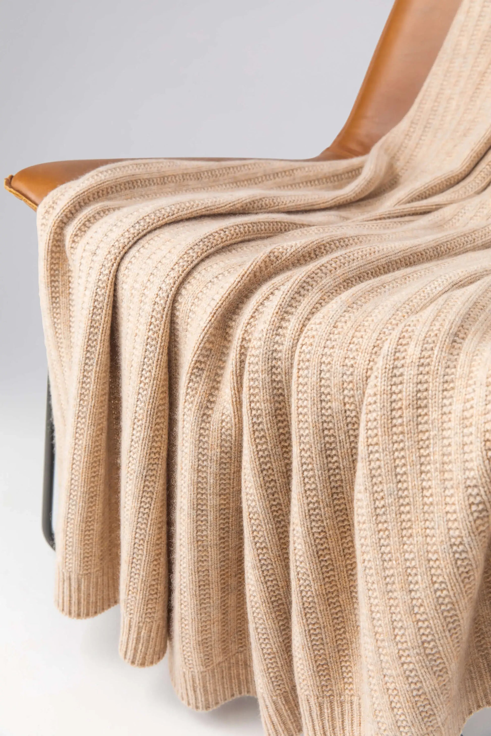 2025 Johnstons of Elgin Interiors Collection Oatmeal Texture Knitted Cashmere Throw draped on a brown leather chair on a grey background  HAI03061HB0254ONE