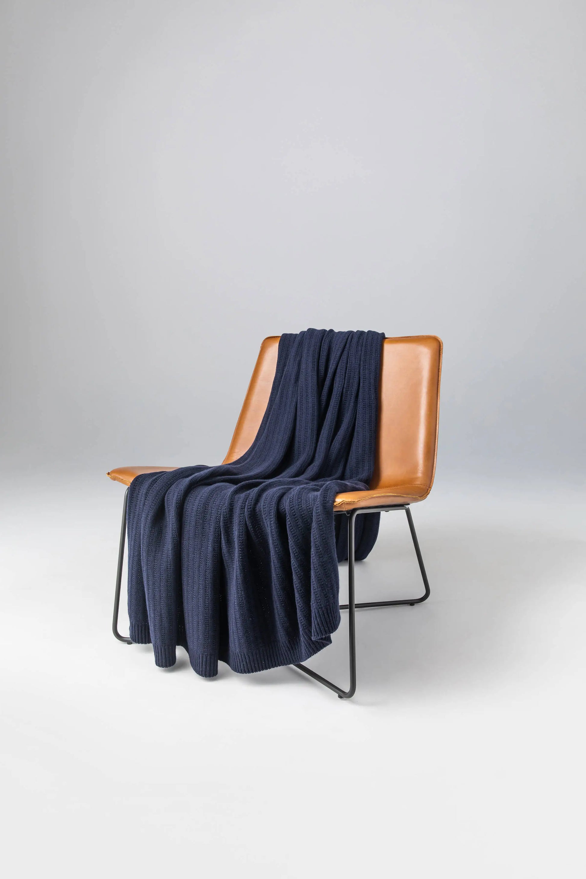 Johnstons of Elgin 2024 Blanket Collection Dark Navy Texture Knitted Cashmere Throw on a leather chair  HAI03061SD7286ONE