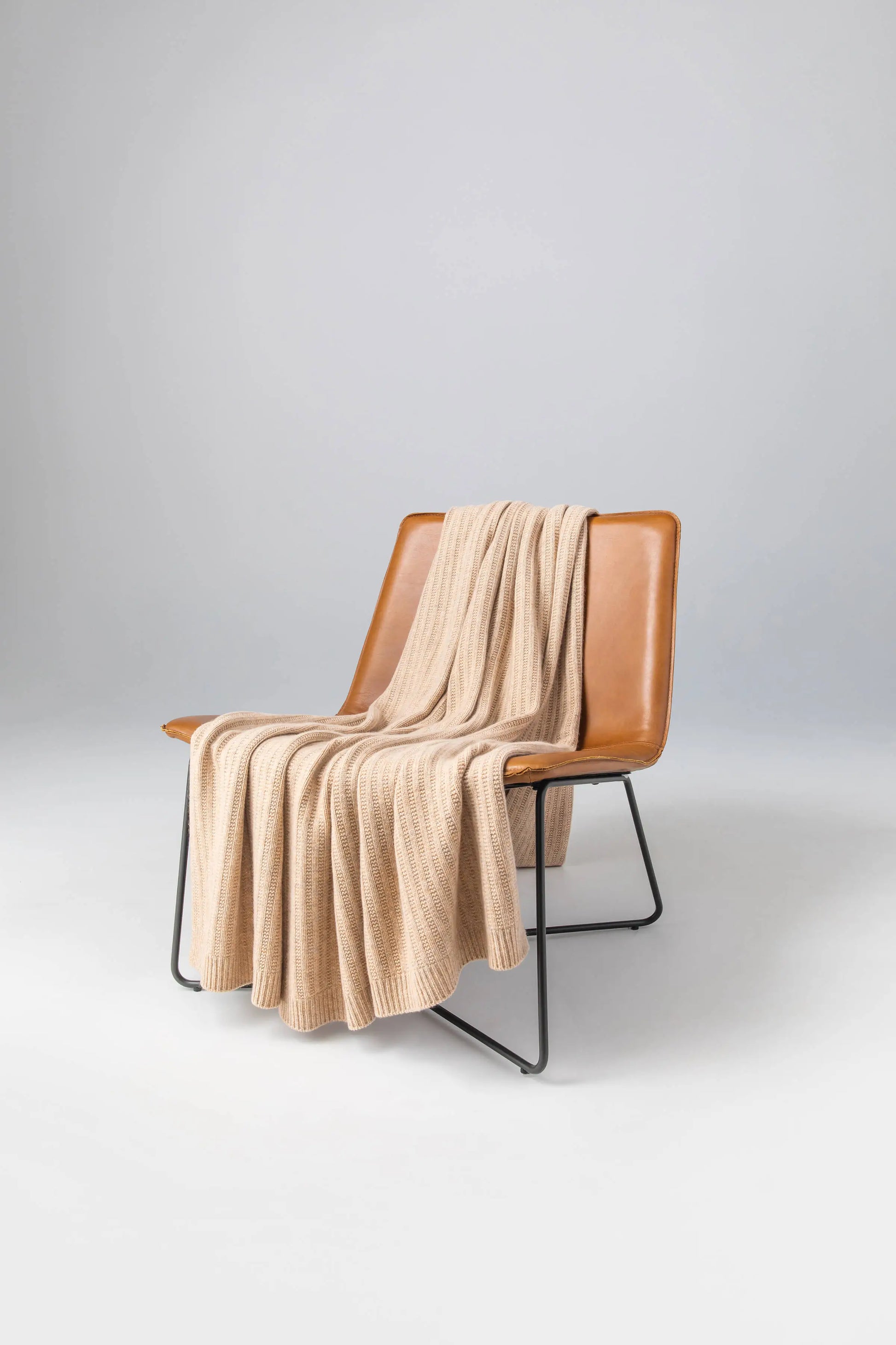 2025 Johnstons of Elgin Interiors Collection Oatmeal Texture Knitted Cashmere Throw draped on a brown leather chair on a grey background  HAI03061HB0254ONE