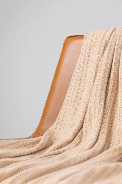 2025 Johnstons of Elgin Interiors Collection Oatmeal Texture Knitted Cashmere Throw draped on a brown leather chair on a grey background  HAI03061HB0254ONE
