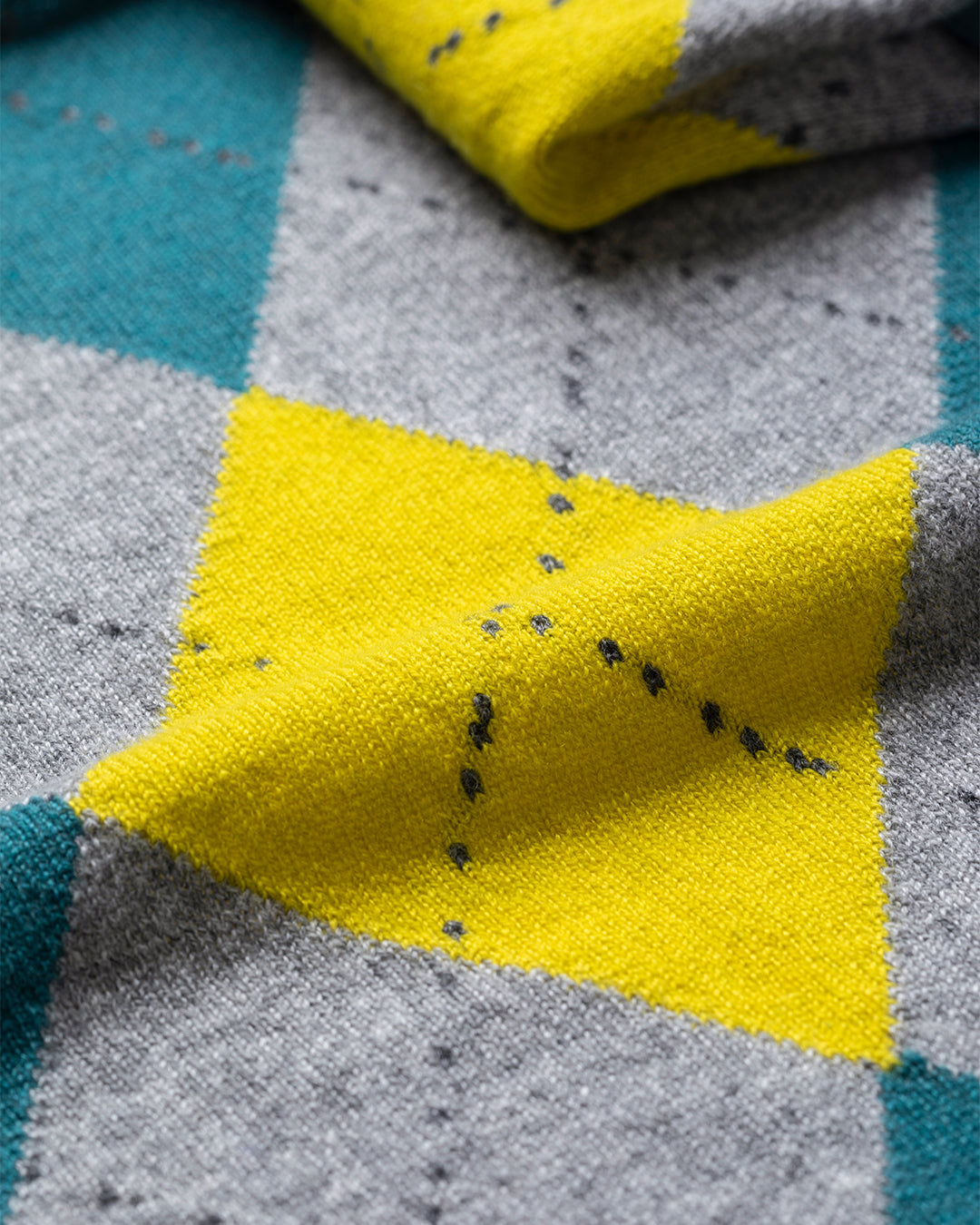 Close-up of a yellow fabric patch with black specks on a gray and blue checkered background. JOHNSTONS OF ELGIN CLAN BANDANA GREY 100% CASHMERE HAP03612JU1615ONE