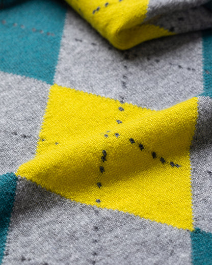 Close-up of a yellow fabric patch with black specks on a gray and blue checkered background. JOHNSTONS OF ELGIN CLAN BANDANA GREY 100% CASHMERE HAP03612JU1615ONE
