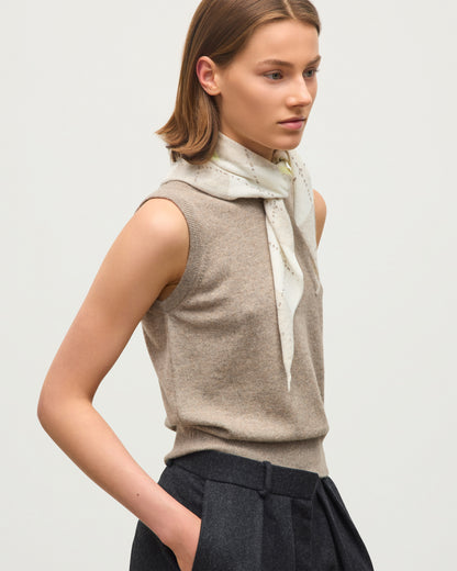 A woman wearing a sleeveless taupe knit sweater vest over a light cream scarf, paired with dark gray trousers, photographed against a clean light gray studio background. JOHNSTONS OF ELGIN CASHMERE NECK TIE ARGYLE CLAN BANDANA NATURAL 100% CASHMERE HAP03612JU1629ONE