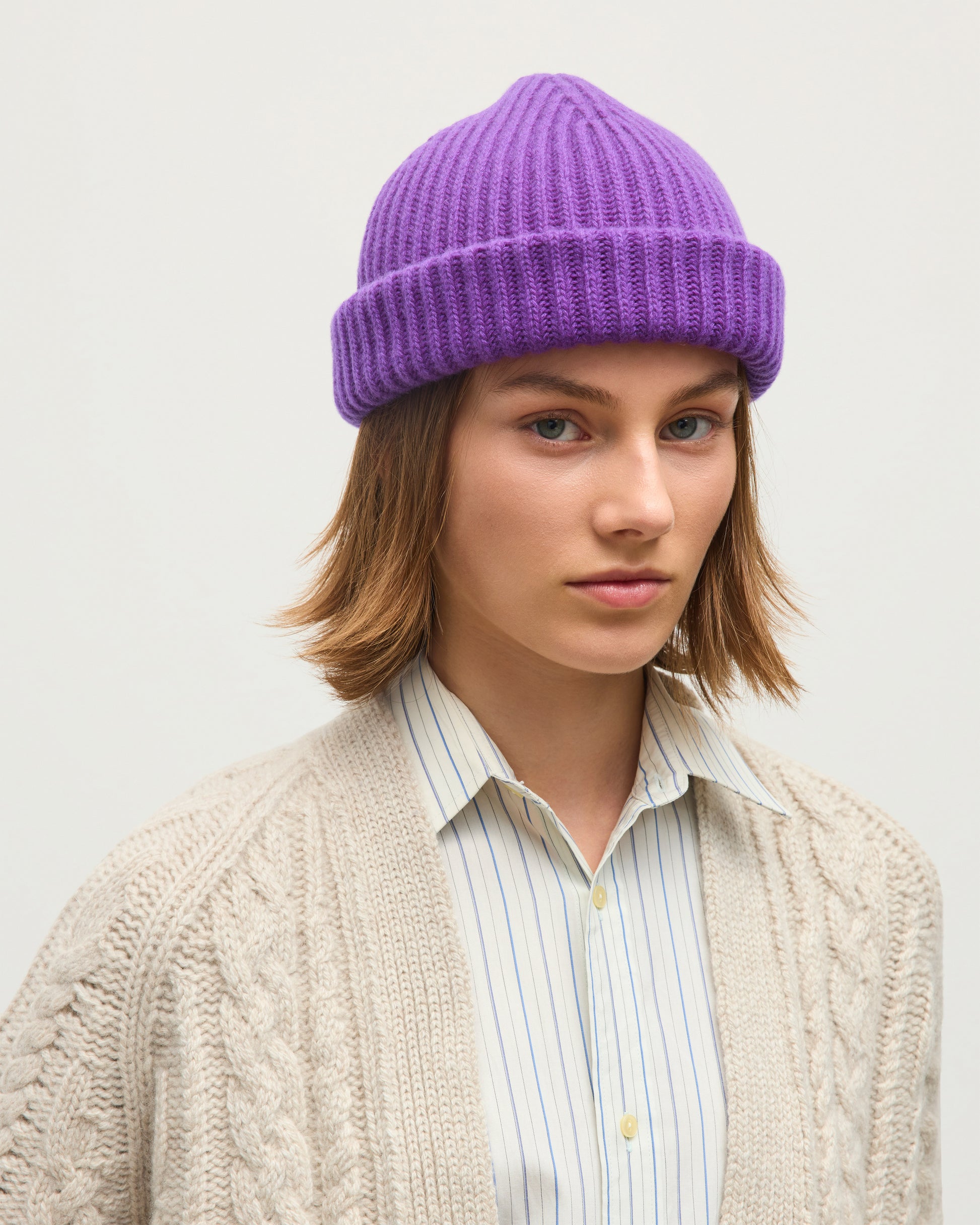 FEMALE MODEL WEARING JOHNSTONS OF ELGIN CASHMERE RIBBED LOVAT BEANIE PURPLE 100% CASHMERE WITH MABEL CABLE CASHMERE CARDIGAN IN WHITE SAND HAY03614SD5371ONE