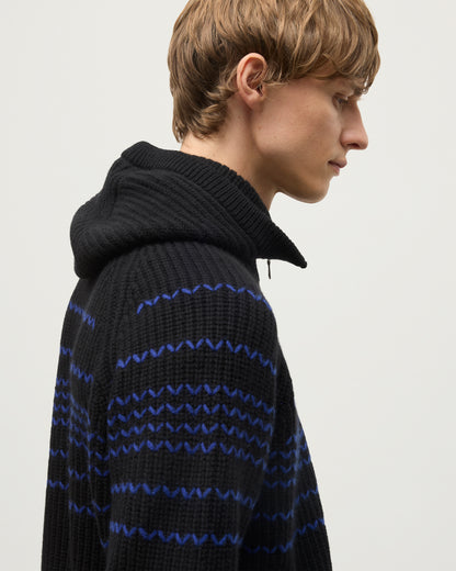 MALE MODEL WEARING JOHNSTONS OF ELGIN NEVIS HOOD BLACK 100% CASHMERE WITH SUMMIT BLACK AND BLUE CASHMERE SWEATER HAY03615Q26168ONE