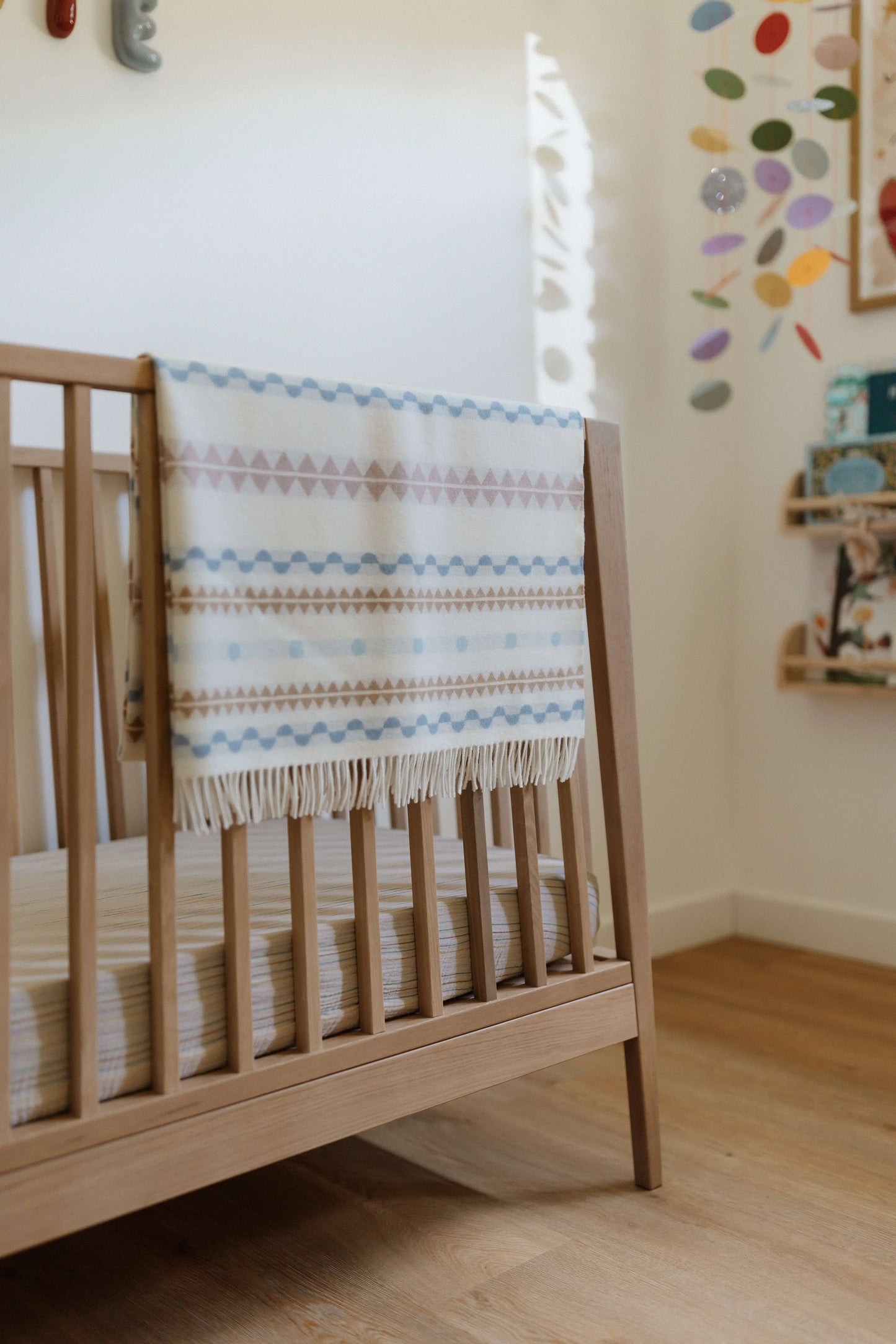 2025 Johnstons of Elgin Interiors Collection Soft Purled Fringe Children's Blanket folded over the side of a wooden cot in a nursery WB002334RU7438ONE