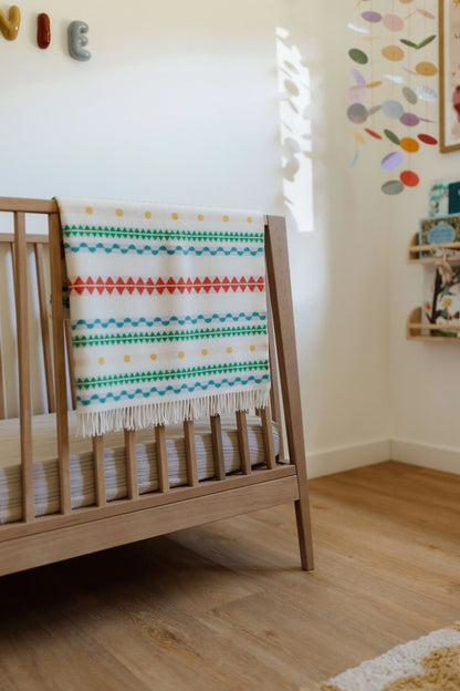 2025 Johnstons of Elgin Interiors Collection Bright Purled Fringe Children's Blanket folded over the side of a wooden crib in a baby's nursery  WB002334RU7436ONE