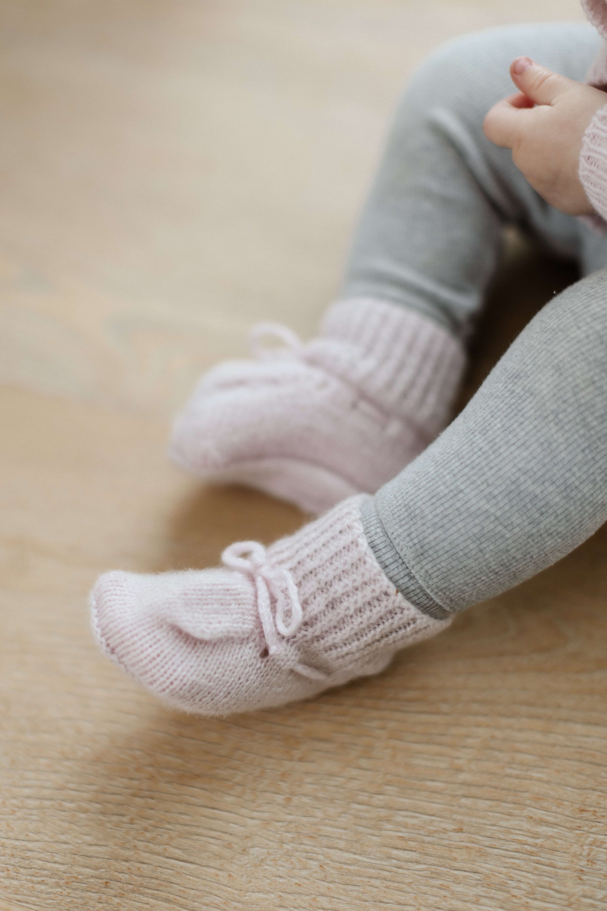 Johnstons of Elgin Hand Knitted Cashmere Baby Booties in Blush on pink check background 61711P191ONE